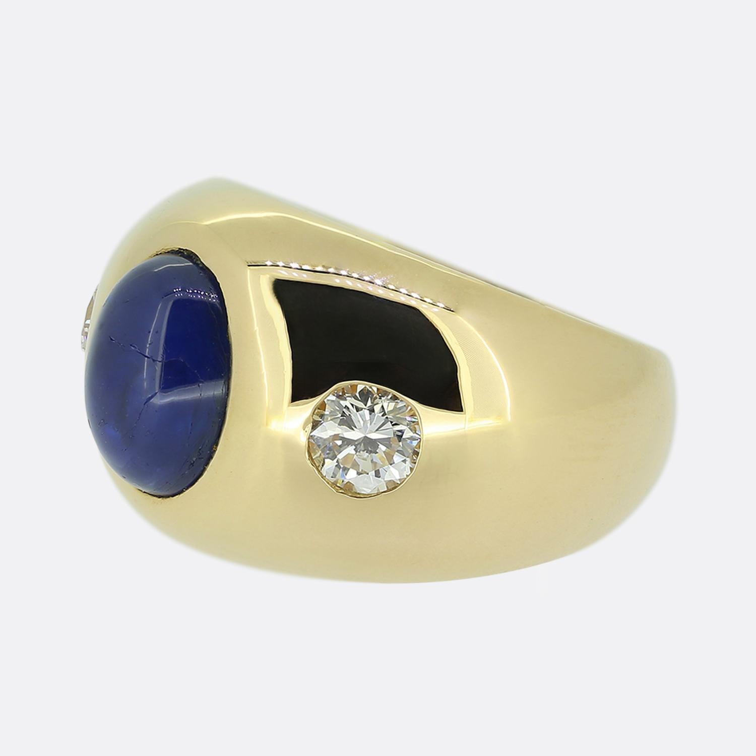 Here we have a chic wide spread ring featuring a trio of precious gemstones. At the centre we find a striking blue cabochon-cut sapphire at its centre which is flanked on either side by a single bright white round brilliant cut; all of which sit