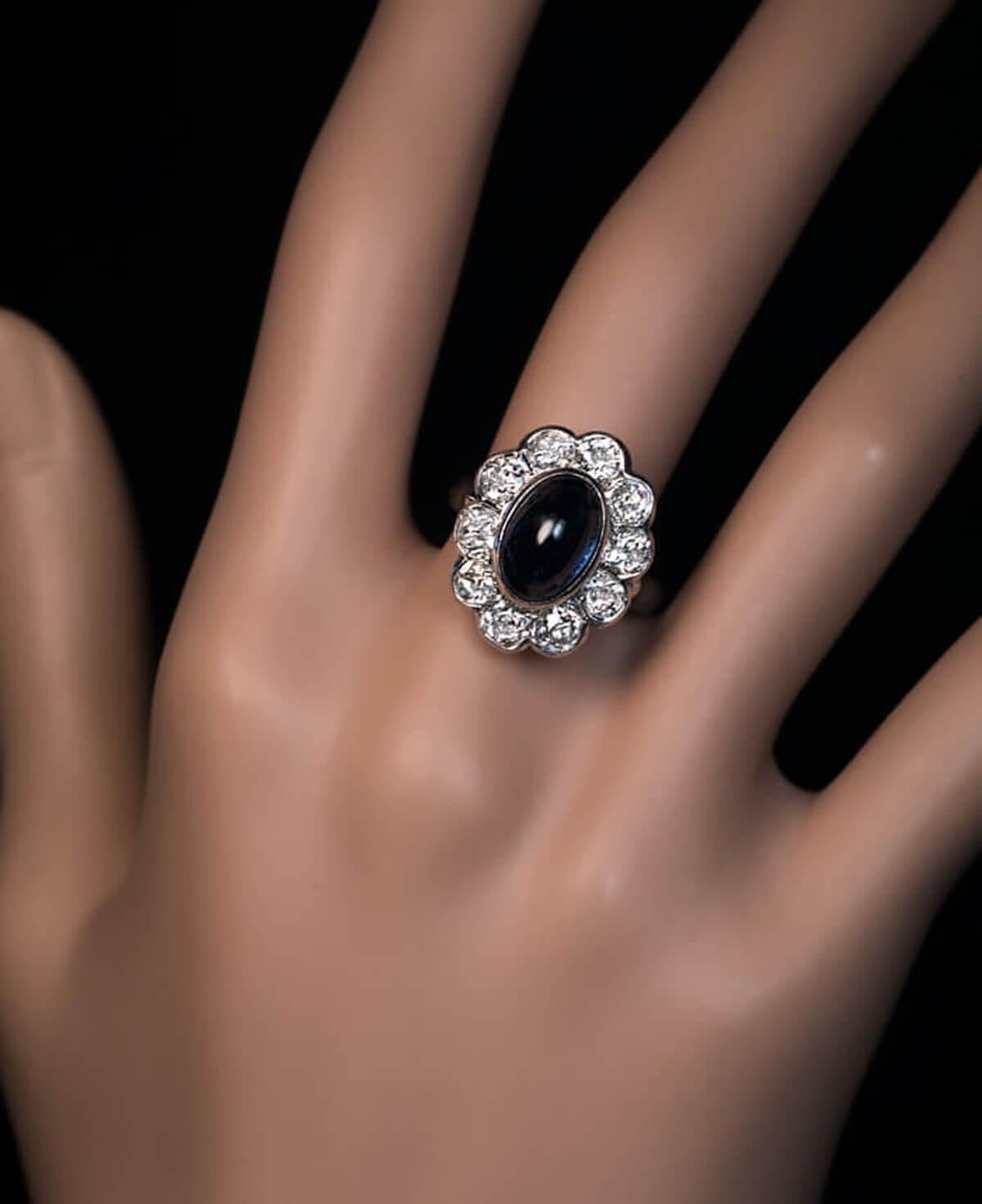 CIRCA 1950  Dieser Vintage-Ring aus Platin ist mit einem mitternachtsblauen Saphir im Cabochon-Schliff besetzt, der von zehn funkelnden Diamanten im Altminenschliff (Farbe H-I-J, Reinheit VS1-SI1) umgeben ist.  Gekennzeichnet mit 900er Platinmarke