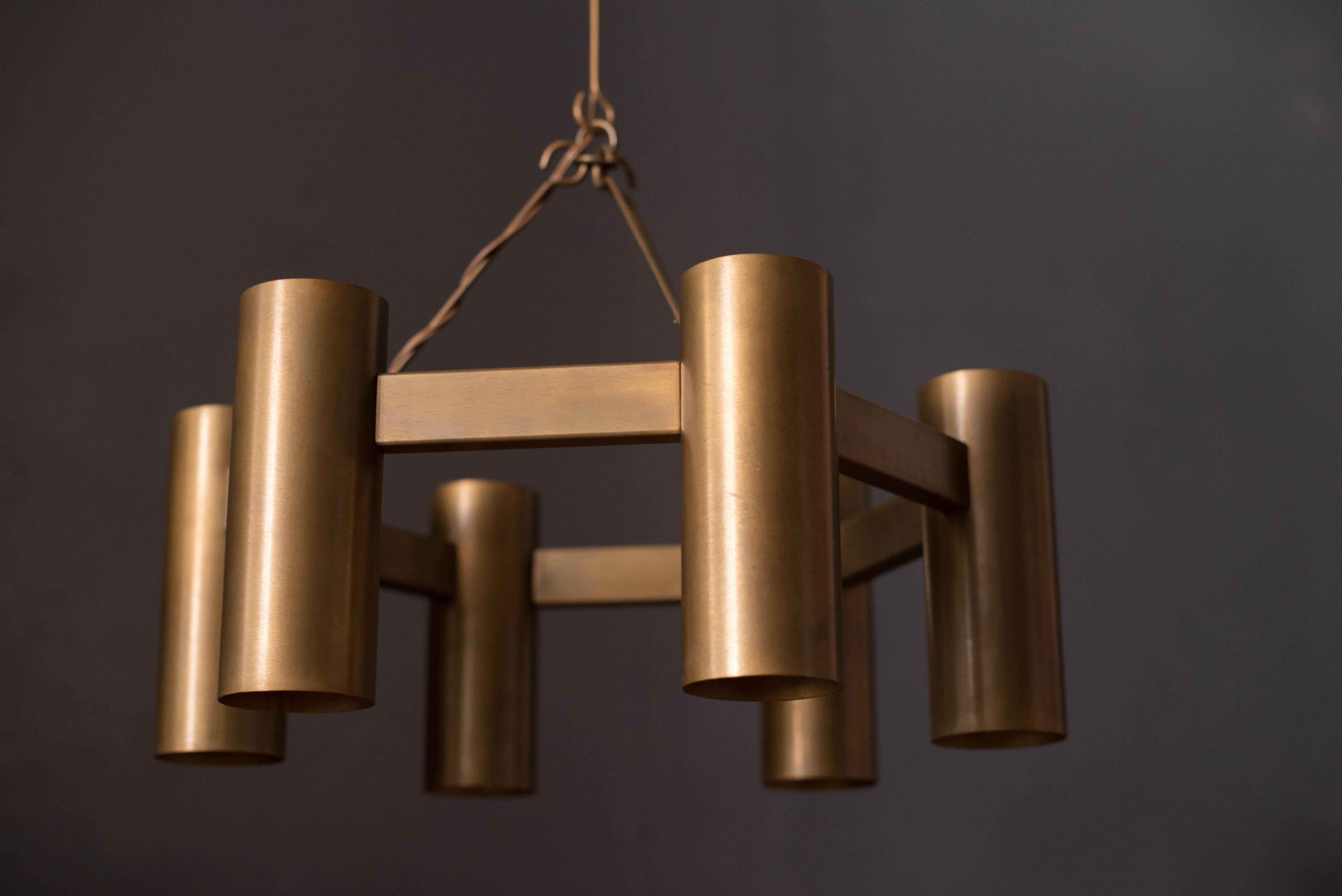 Mid Century industrial modern chandelier fixture by Stuart Barnes for Robert Long, circa 1960s of Sausalito, California. This piece features aged brass and includes six cylinders that expose light from the top and bottom. Includes two 12