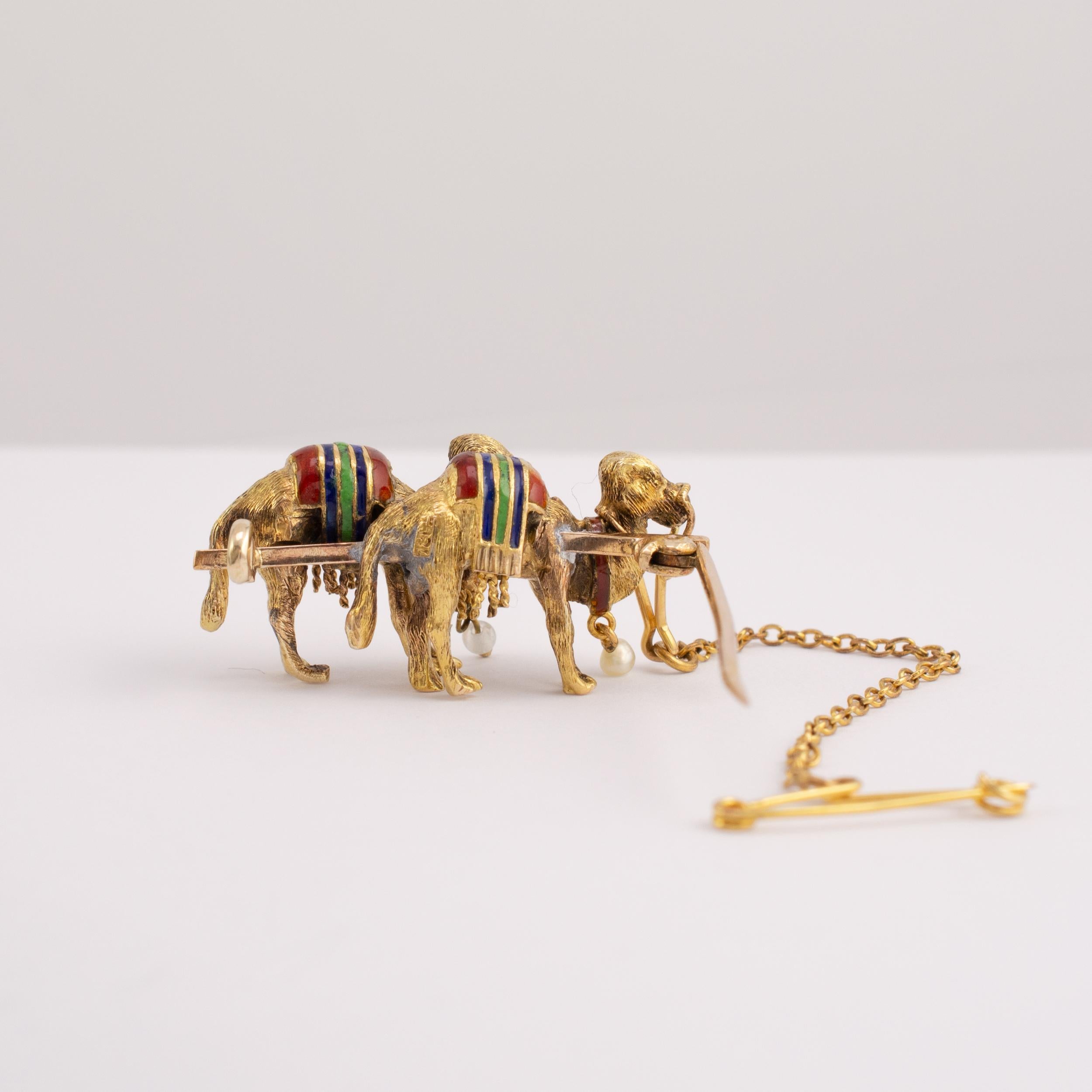 Vintage 18 karat gold camel brooch with pearl drop and enamel decoration, Circa 1940s.

The camels are finely detailed with a textured finish. Each camel is decorated with red green and blue striped enamel rug seat with gold tassels. Under one camel