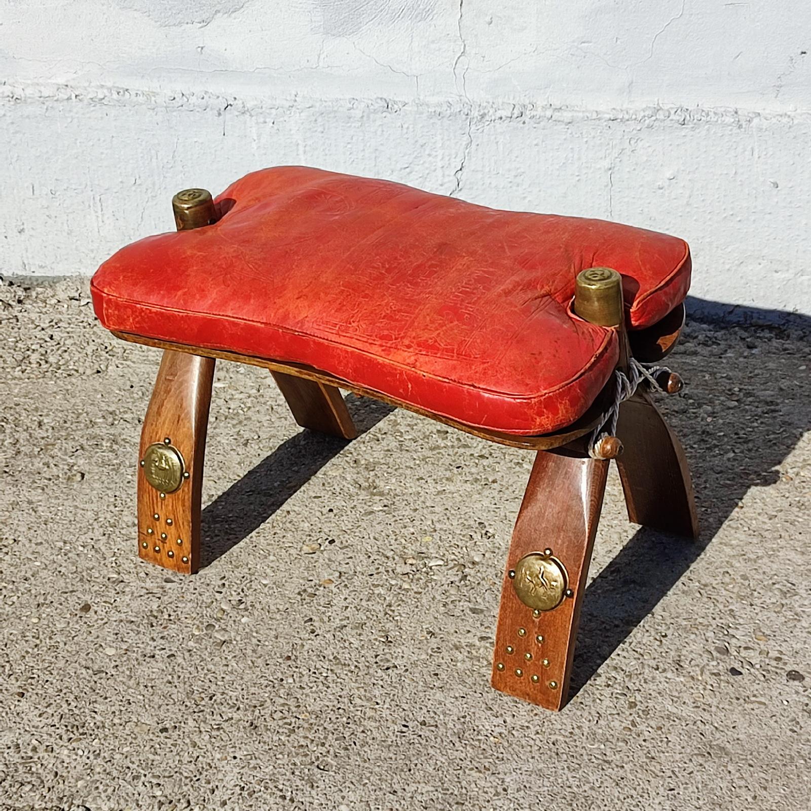 A Vintage camel leather saddle stool ottoman, Morocco C.1960.
Camel stool with raw hide rope ties. The cushion in red leather with embossed drawings, filled with seagrass. Golde trim accents on feet and at the top of sides.
Measures: 56 x 33 x 39