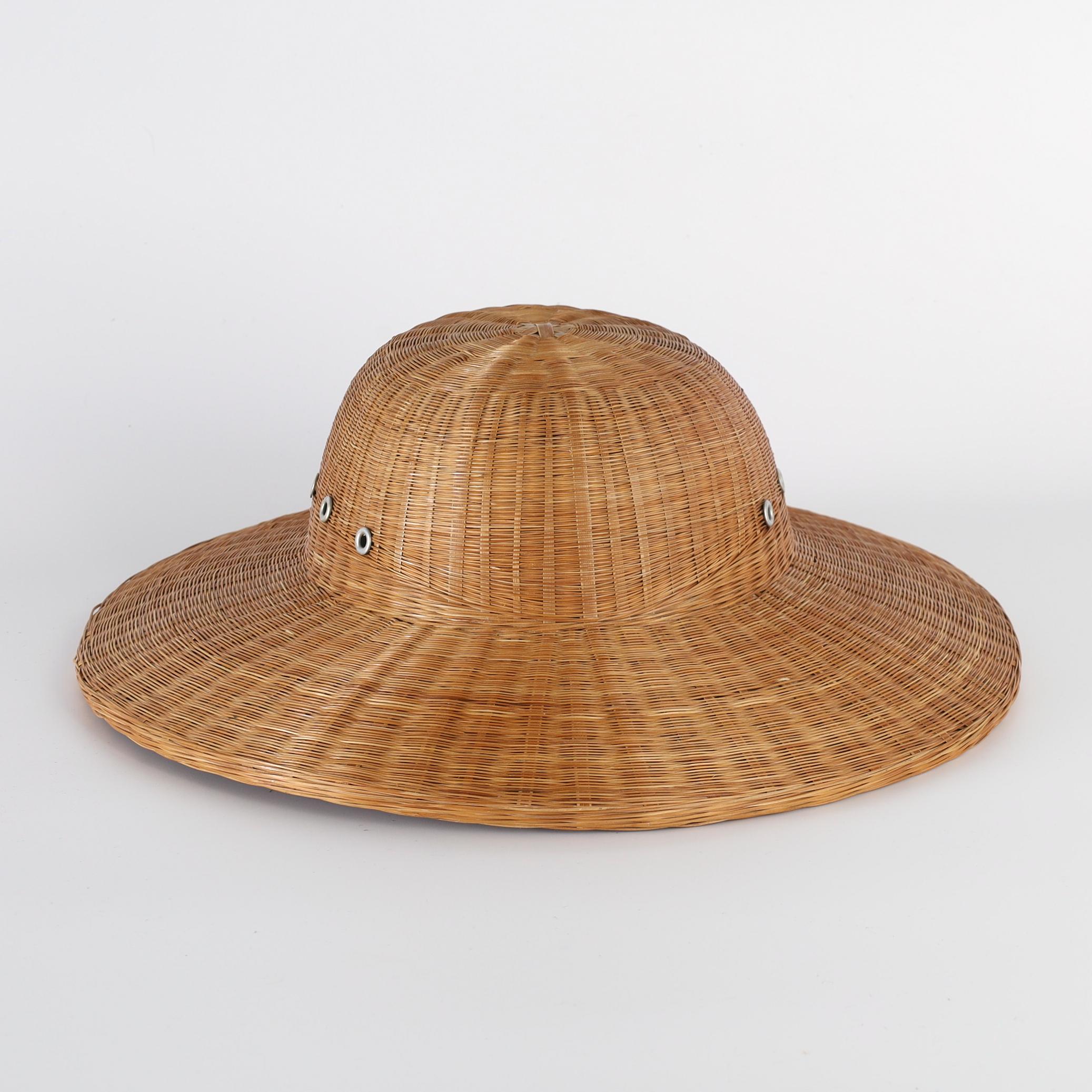 Transporting British Colonial Anglo Indian pith helmet or hat ambitiously handcrafted in woven reed or wicker in classic form with metal breather holes and plenty of tropical charm. By Shanghai Handicrafts.