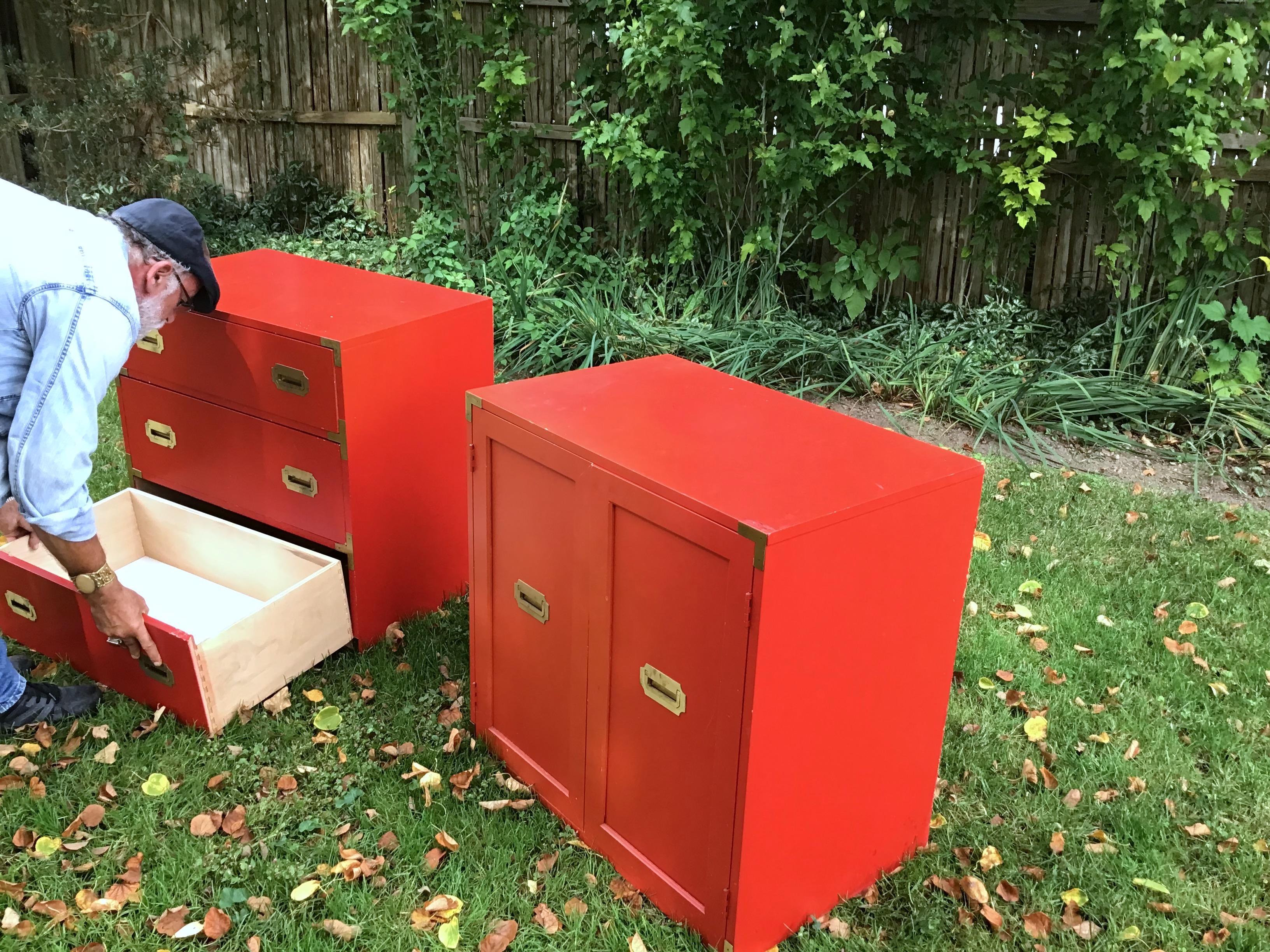 A pair of orange/red campaign chests with brass details can be used as night stands. They are in good condition, but have some wear at corners.