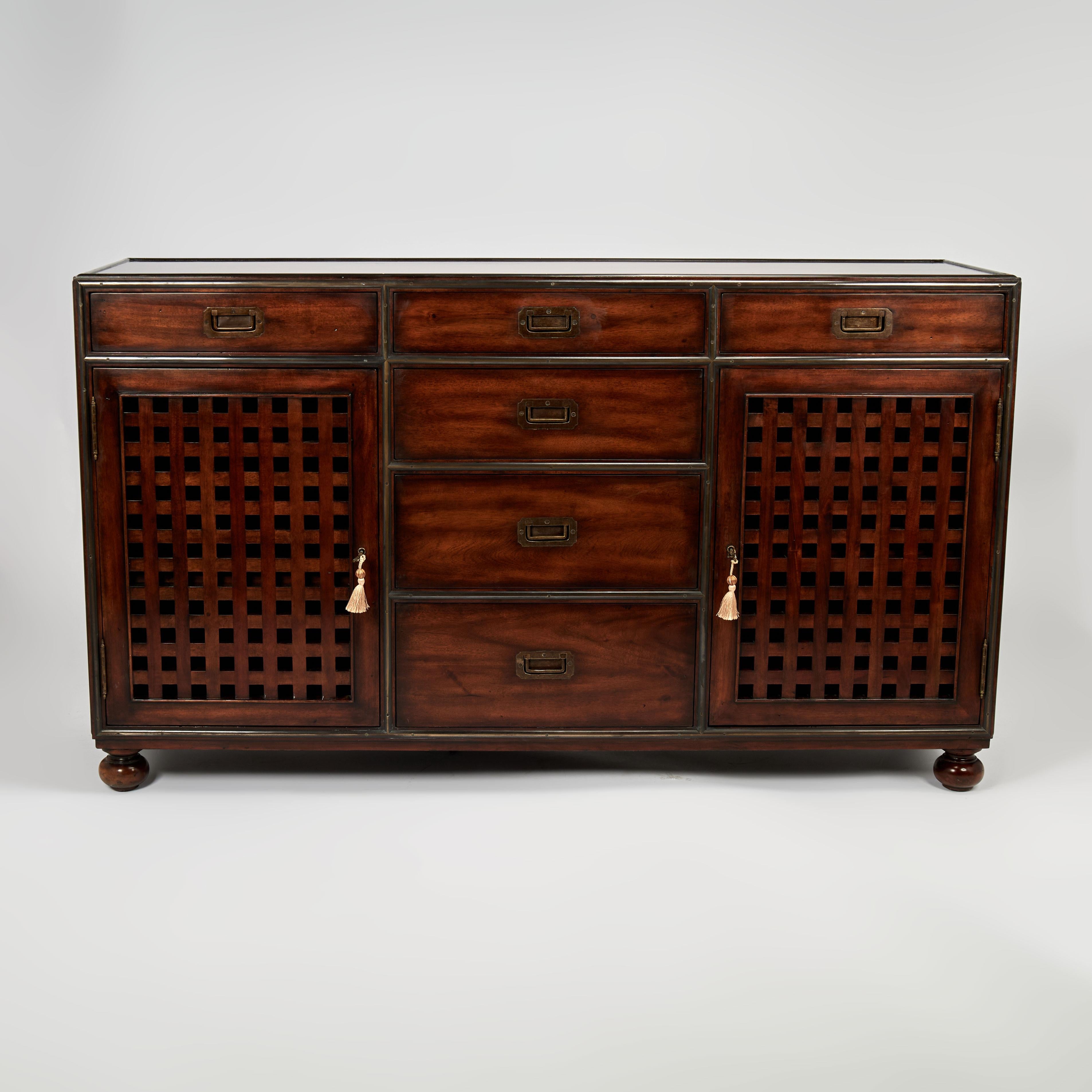 Handsome mid century chest crafted in mahogany with campaign style brass banding and hardware, having six drawers and two cabinets with geometric open fretwork and standing on classic turned feet. Signed Theodore Alexander in a drawer.