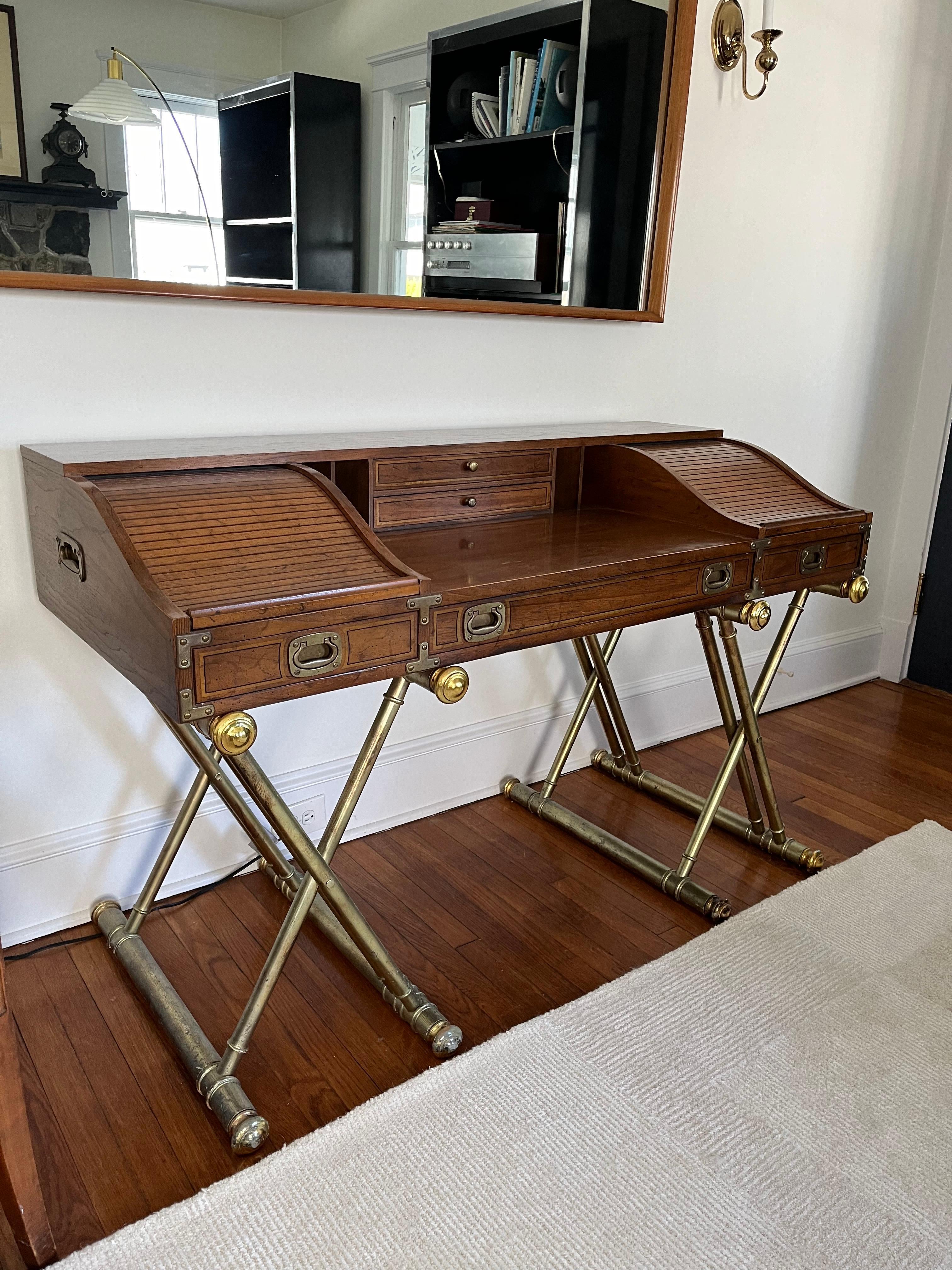 Campaign style desk designed by John Van Koert for Drexel. The desk is supported by gold crossed wood supports with a gilt finish. The top portion offers cubby-hole storage on either end which is hidden beneath rolling tambour doors. Behind the