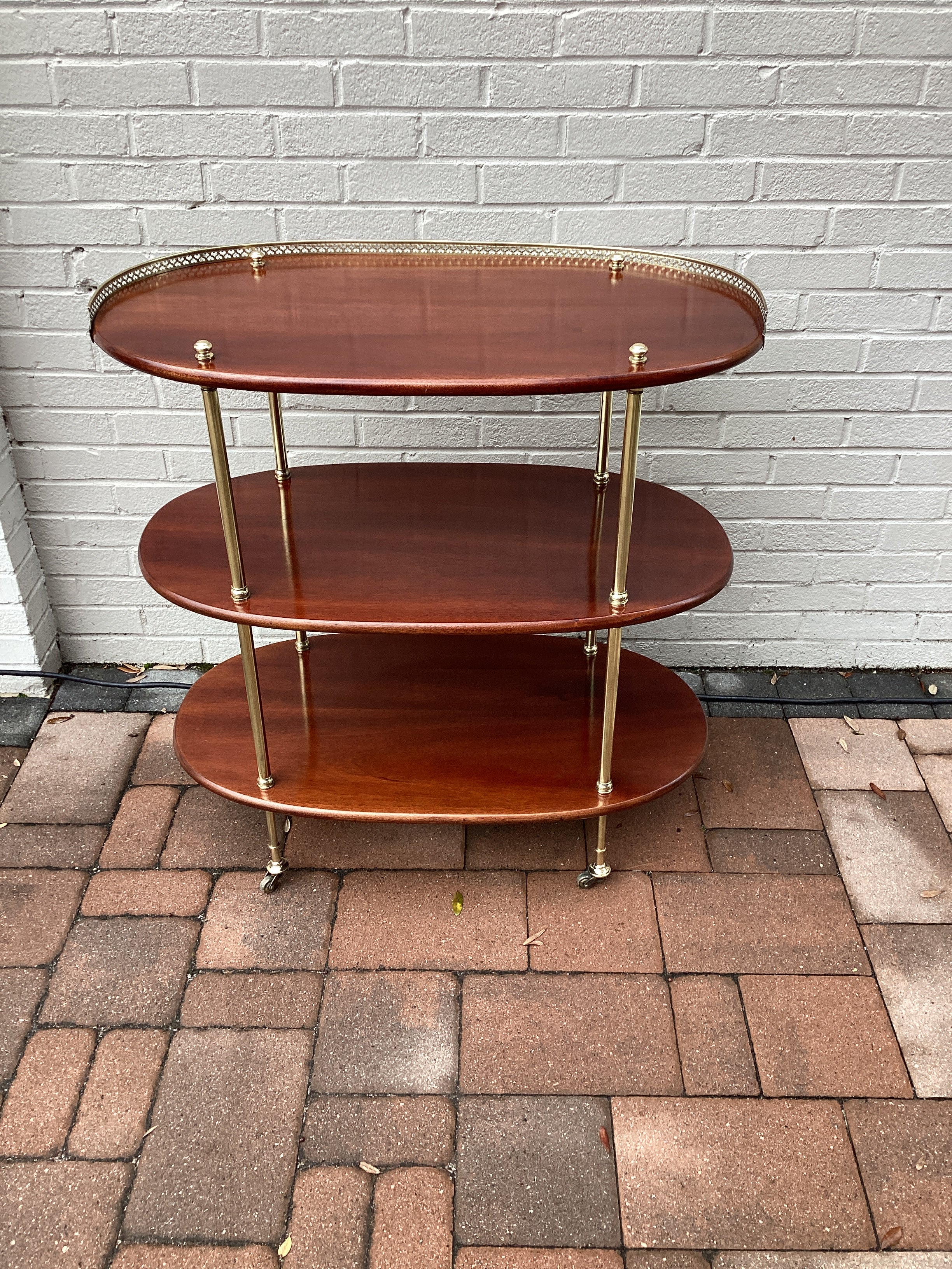 Vintage British Campaign style side table or bar cart with three oval mahogany tiers, top tier with a pierced brass gallery, each tier separated by brass support. Table rests on castors.  Completely restored.