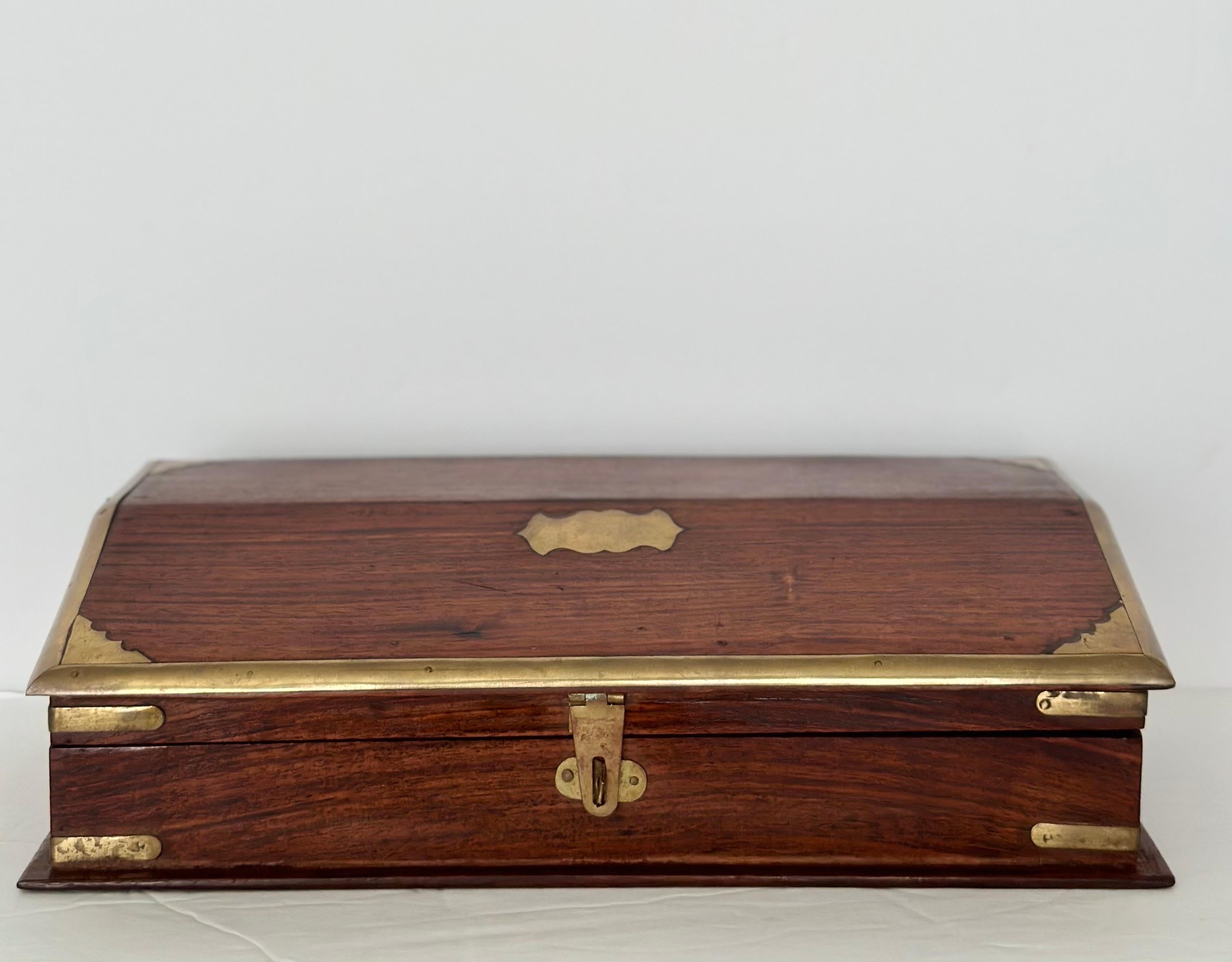 We are very pleased to offer a timeless campaign-style wood box, gracefully adorned with brass inlays, circa the 1950s.  The exterior of the box reveals the natural beauty of the wood, contrasted beautifully with the intricate brass designs that are