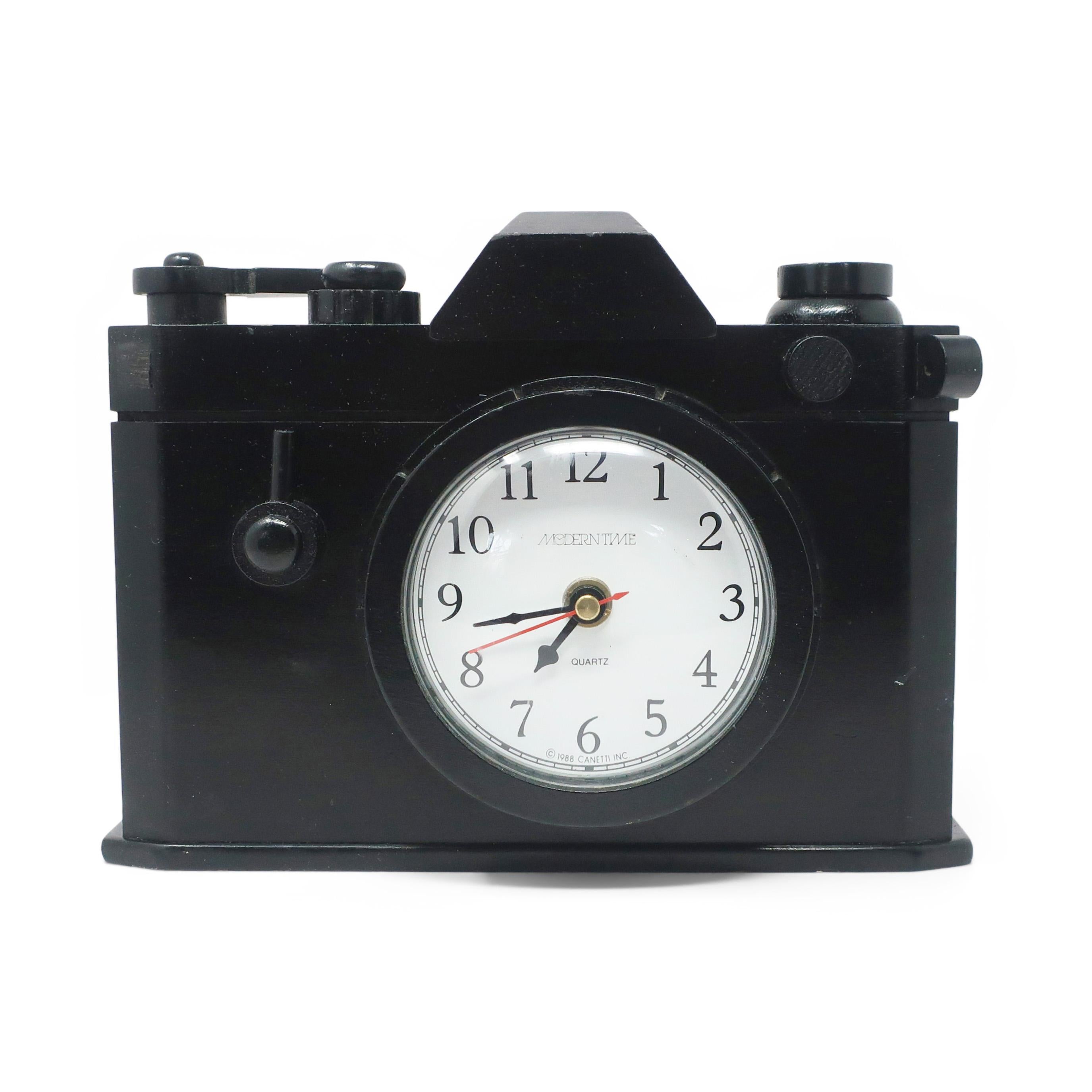 A postmodern clock by Canetti in the shape of a camera.  The clock's face is set into the camera's lens and the body is solid wood with a moving film advance lever. In vintage condition with wear consistent with age and use, including two small wood