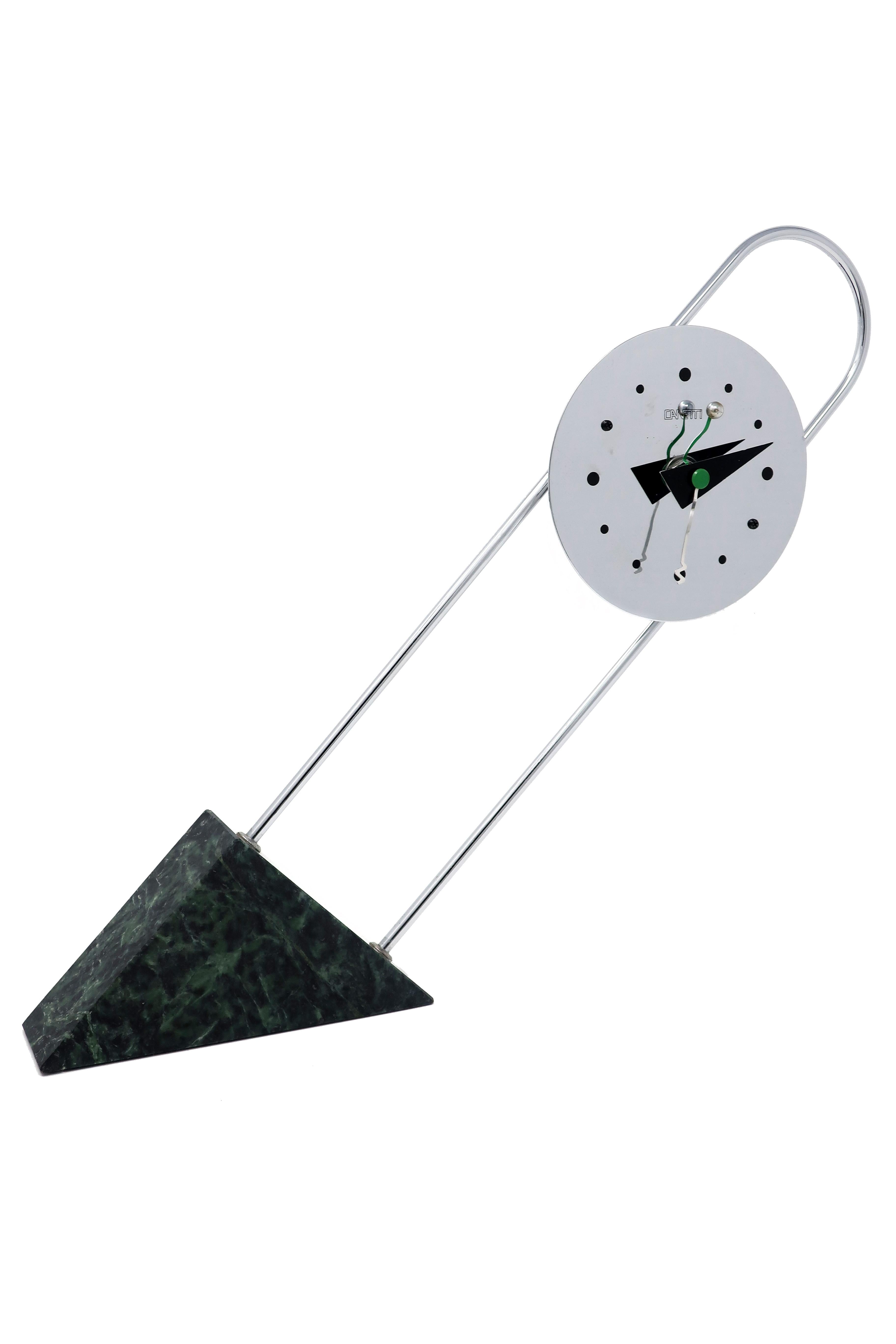 A stunning Postmodern clock by Canetti with a chrome face on an arching chrome stem set at an angle into a green marble base. Dated 1989, this clock screams its Memphis inspiration from the use of primary shapes to the quirky shapes of the clock’s