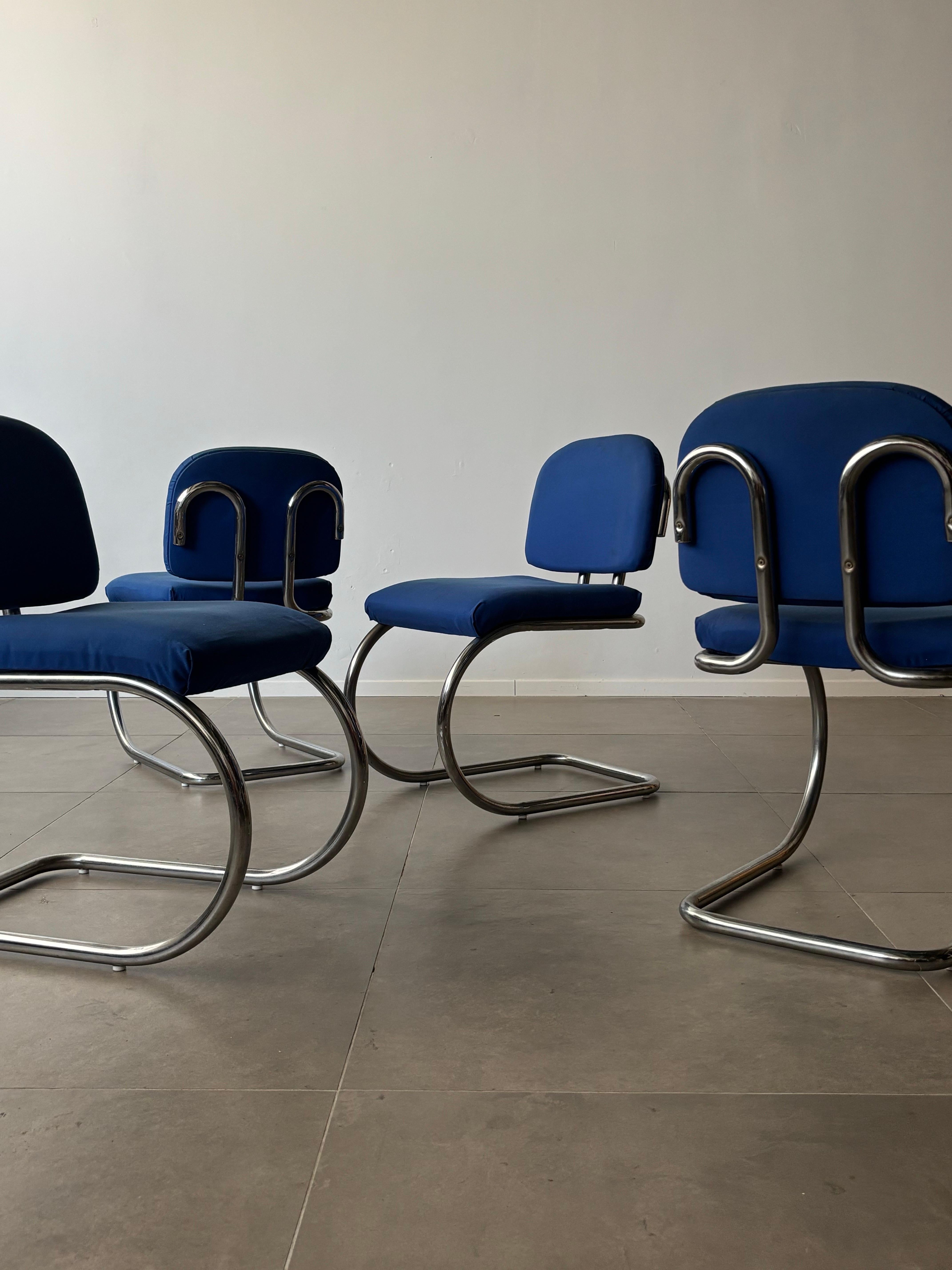 Vintage cantilever chairs with a Bauhaus-inspired design, featuring a chromed steel frame and blue fabric upholstery. The frame elegantly curves away from itself as it meets the backrest, creating the chairs’ most distinctive design