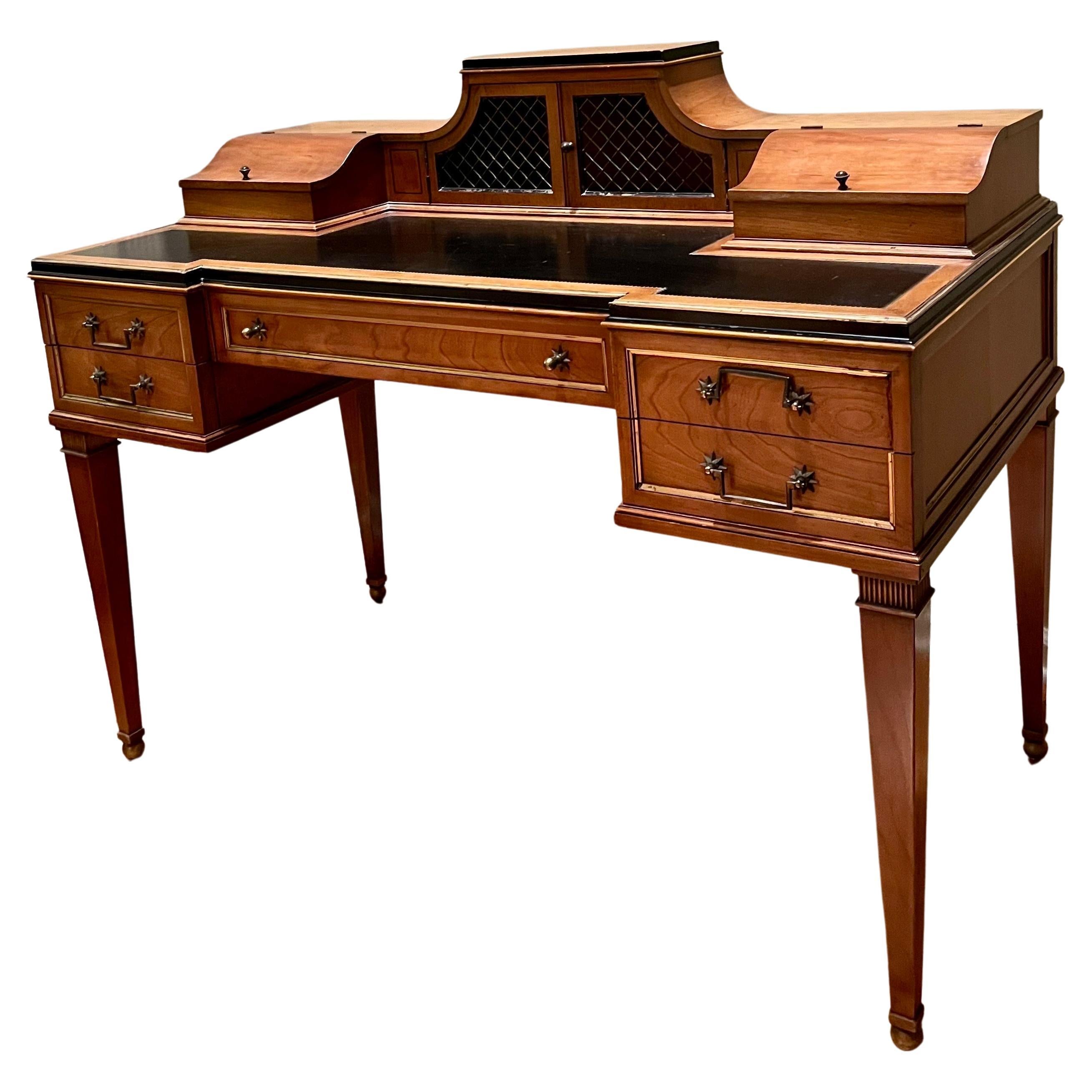 Carlton House Writing Desk. Stands on four hepplewhite legs with ball feet. Accented with tooled leather top, starburst brass drawer pull, brass trim on all sides and drawers. Metal fretwork cabinet doors. Features multiple drawers, compartments and