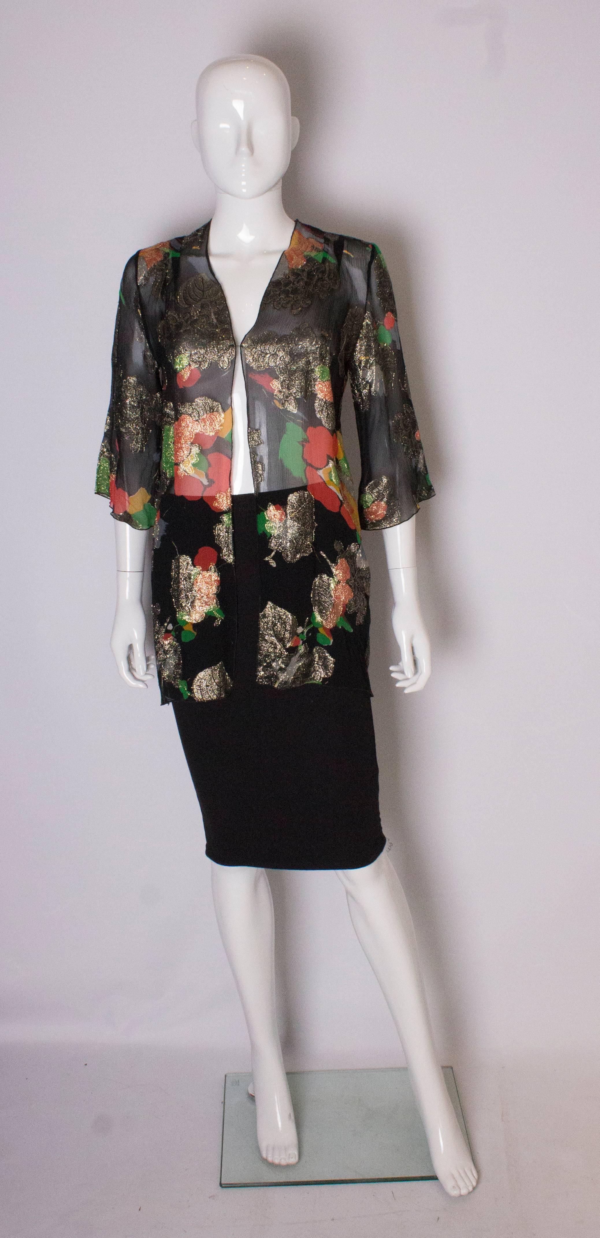 A chic and easy to wear evening jacket by Caroline Charles. The jacket is in black silk, with colour and lurex detail. It has elbow length sleeves and two pleats on the shoulder