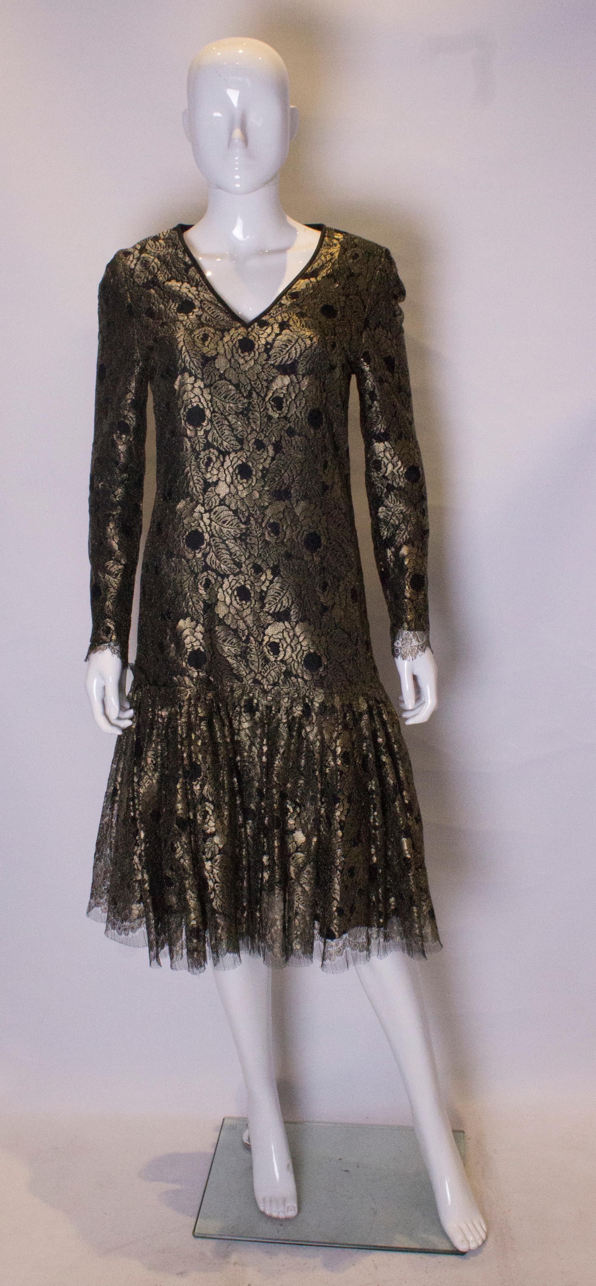 Das schicke Kleid von Caroline Charles ist aus goldener Spitze gefertigt und schwarz gefüttert. Es hat eine fallende Taille mit einer Rüsche am Saum und einen zentralen Reißverschluss am Rücken.