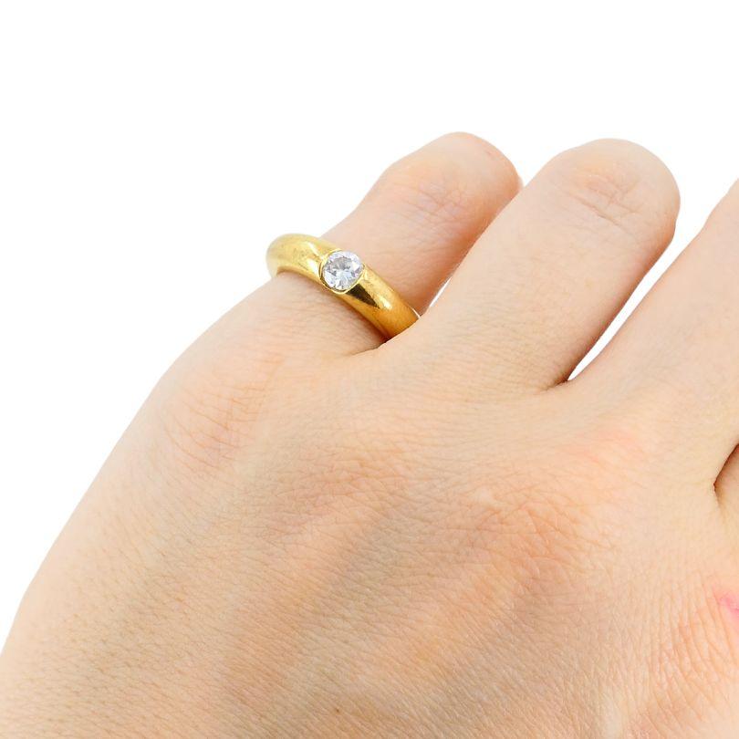 This vintage Cartier diamond band ring, crafted in 1993, is made of 18k yellow gold and features a minimalist design. The central round brilliant-cut diamond is set flush within the band, providing a sleek and secure look. The band itself measures