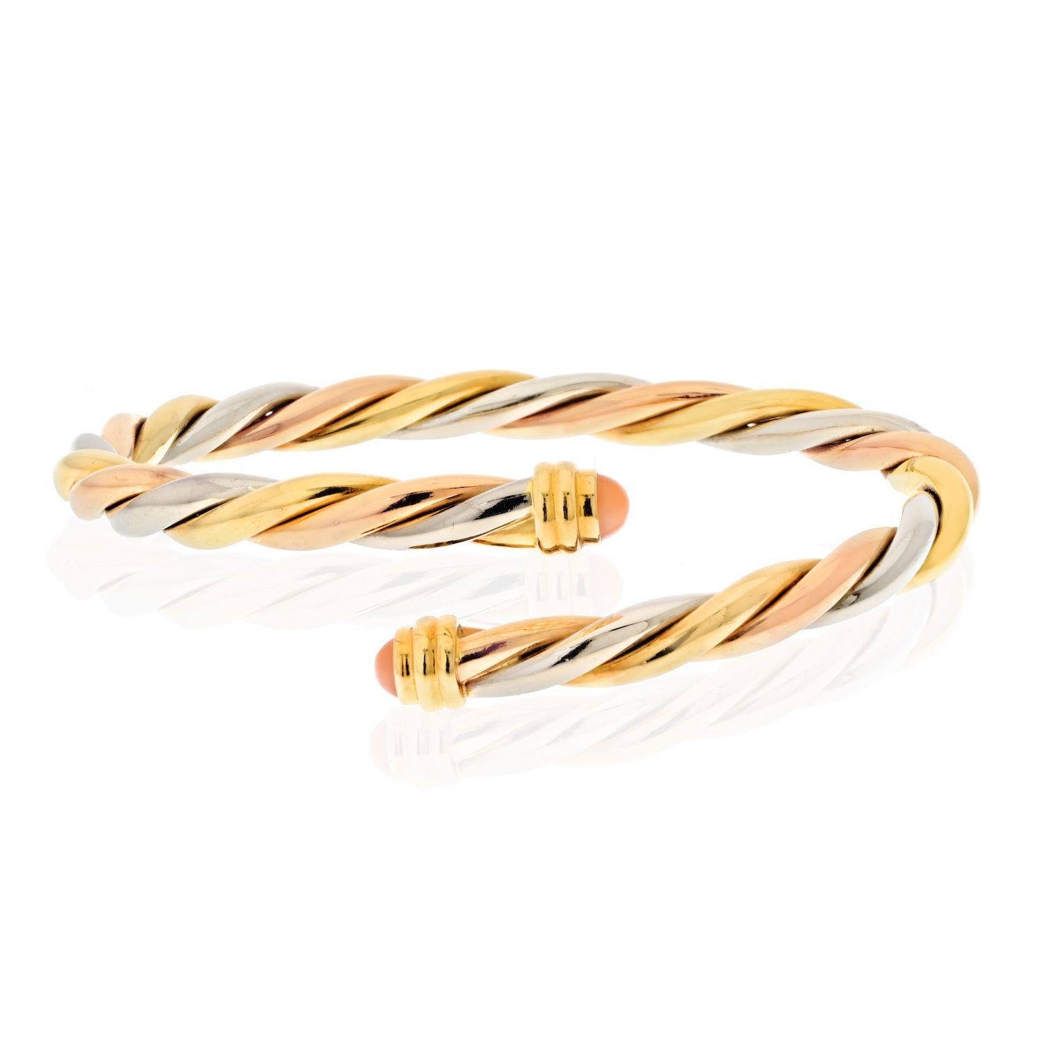 This Cartier vintage bangle is made of three tone 18 karat gold, including yellow, white, and rose forms a twisted braid accented with coral cabochon ends. Wrist size 6.5 inches. EU size 17cm. 