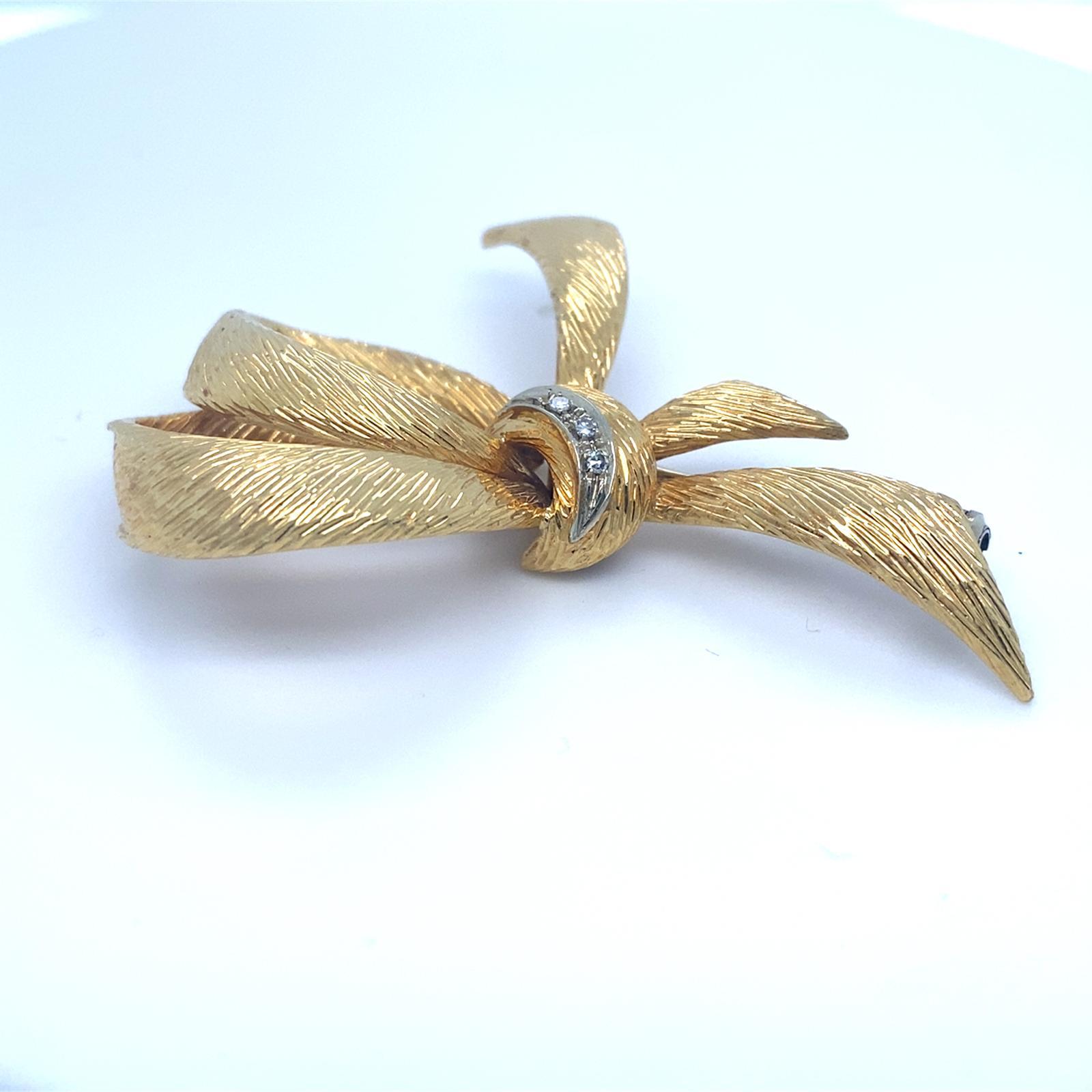 Gorgeous textured 18k yellow gold bow brooch by Cartier.
Features a white gold accent with three small diamonds.
Made in France.
Piece is in good condition. Shows few signs of aging or wear.

Length: 2.25 inches.
Metal: 18k yellow gold, 18k white