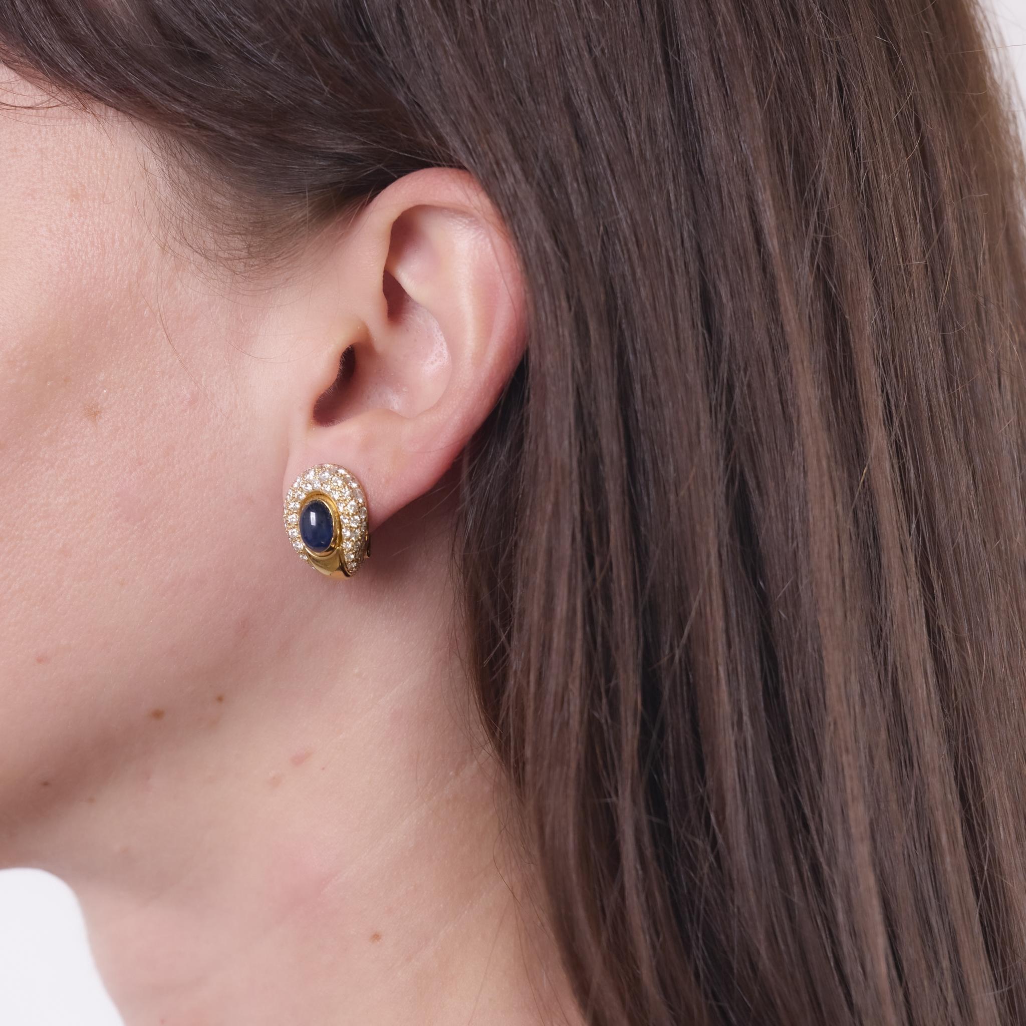 These vintage Cartier earrings from the 1990s are crafted in 18k yellow gold and feature two cabochon cut sapphires totaling approximately 4.65 carats. Surrounding the vibrant sapphires are 116 round brilliant cut diamonds, totaling approximately 3