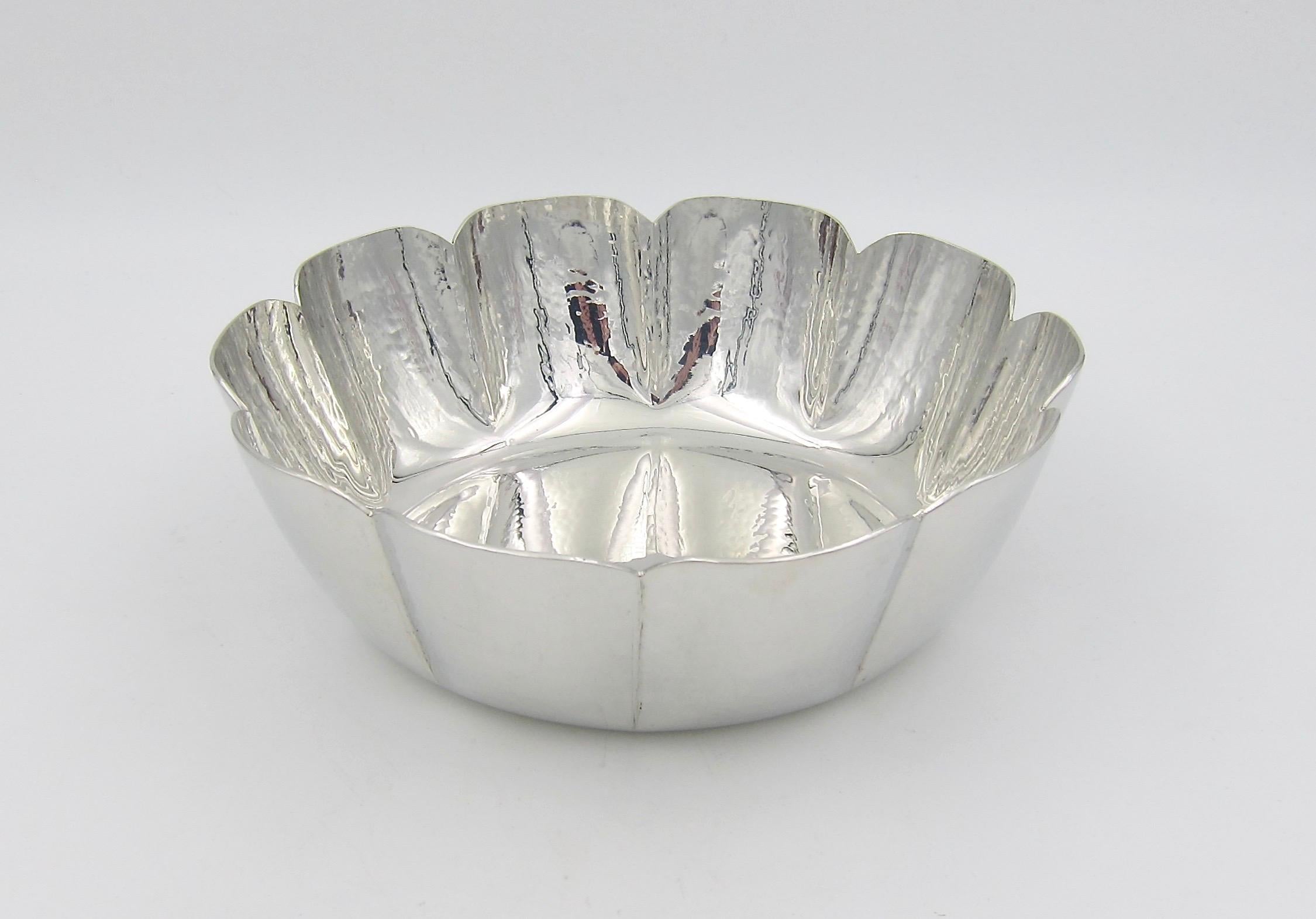 A vintage Cartier bowl handcrafted of polished pewter with a hammered surface dating to the 1980s. The elegant lobed design in highly reflective silver metal has fluted edges flaring outward to a scalloped rim, measures: 7.75 in diameter (at