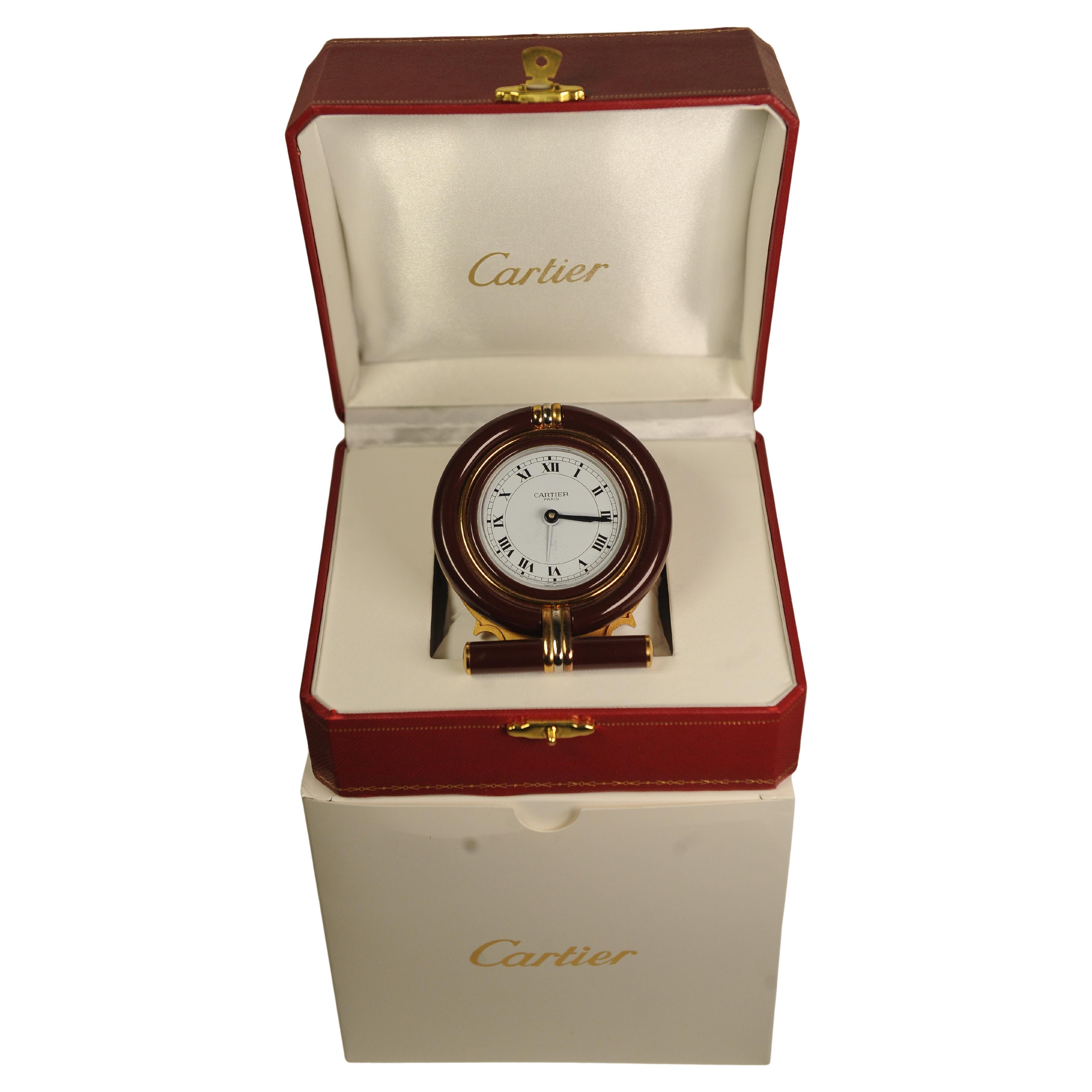 Un elegante orologio da tavolo con movimento al quarzo circolare di Cartier Sveglia da tavolo in metallo dorato e smalto marrone con quadrante bianco e numeri romani 

Fornito con una scatola rossa. 

Orologio Made in Switzerland Numero 752205187

-