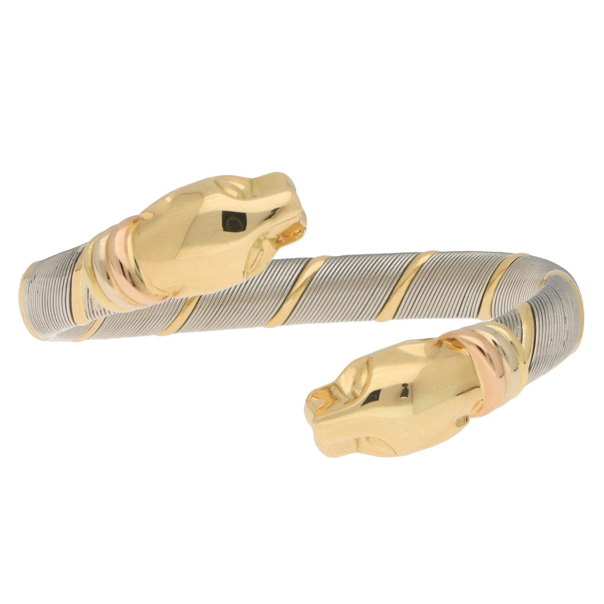 A beautiful vintage 1980’s Panthère de Cartier bangle set in stainless steel and 18k tri coloured gold. 

This incredibly stylish bangle is composed of two solid yellow gold panther heads. These heads are connected to a coiled stainless steel and