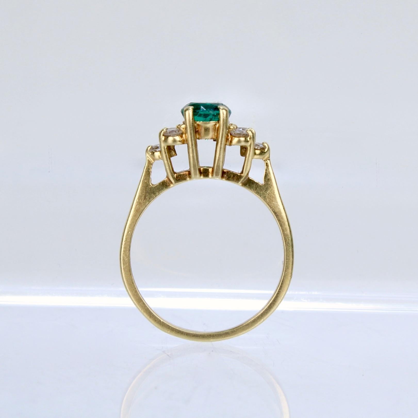 A wonderful Cartier 18k gold, diamond and emerald cocktail ring.

With a round-cut emerald set at its center and flanked on each side by a cluster of 3 white diamonds. 

Each stone is prong set above a gallery with openwork. 

Simply a wonderful