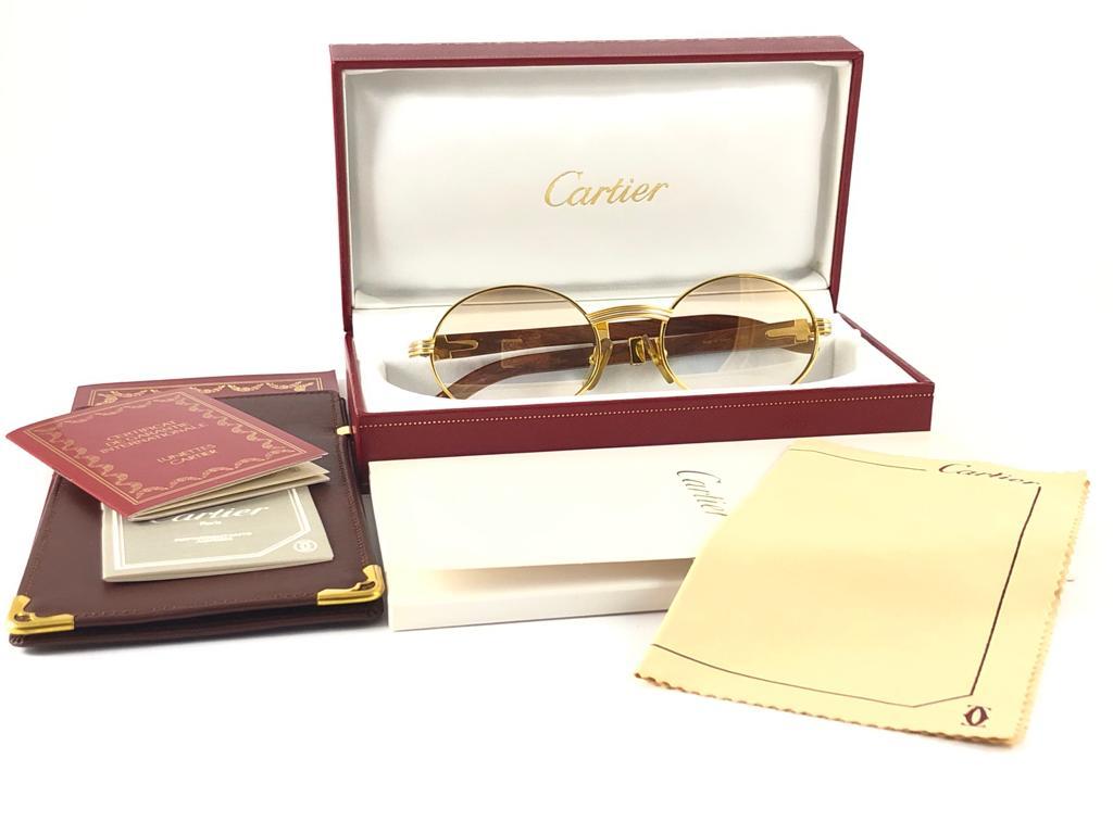 Seltene Original Cartier Sonnenbrille aus Gelb- und Weißgold von 1992 mit Palisanderbügeln und hellbraunen Verlaufsgläsern.  
Rahmen mit Front und Seiten in Gelbgold.  
Alle Markenzeichen.  Goldene Cartier-Zeichen auf den Ohrmuscheln. 
Beide Arme