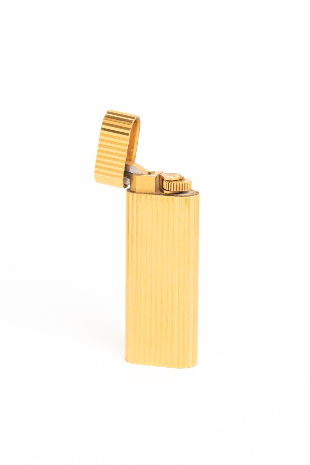 Classic and elegant Must De Cartier Stripe Gold Plated Lighter with original red Cartier pouch, Cartier extractor + instruction booklet for lighters. The bottom of the lighter is stamped 'Cartier', 'Paris', and 'SWISS MADE' with serial number:
