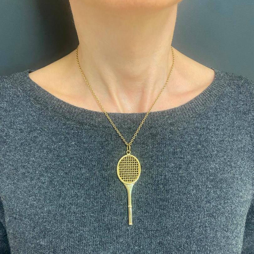 A vintage Cartier necklace, featuring a 14k gold tennis racket pendant and an 18k gold chain.
The tennis racket pendant was crafted with attention to the grid of the strings and a smooth, elongated handle, that gives it a realistic look. The 18k