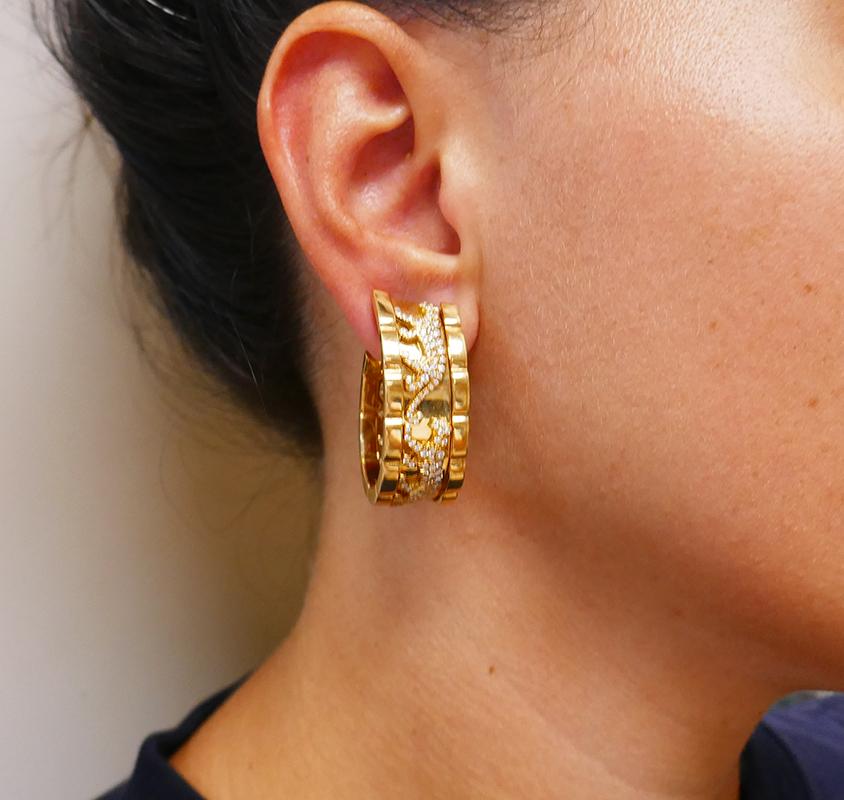 An iconic pair of vintage Cartier Panther earrings.
These “Panthère de Cartier” gold earrings are designed as a wide hoop depicting three walking panthers. The latter are embellished with pave diamonds. Two cats are set outside, and one is placed