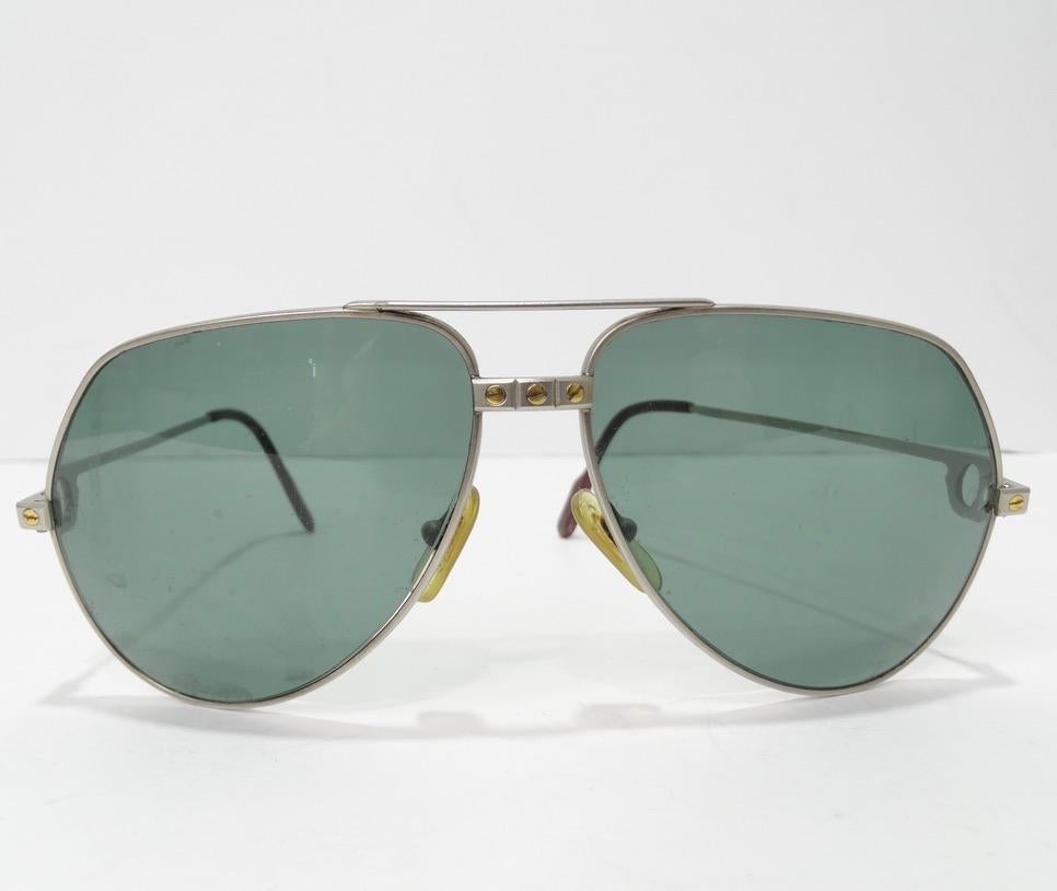 Cartier aviator style sunglasses featuring Cartier's signature titanium screw motif circa 1980s. Thin silver frames with solid yellow gold screws are complimented by tinted UV protectant lenses. Ear paddles feature red enamel with gold Cartier