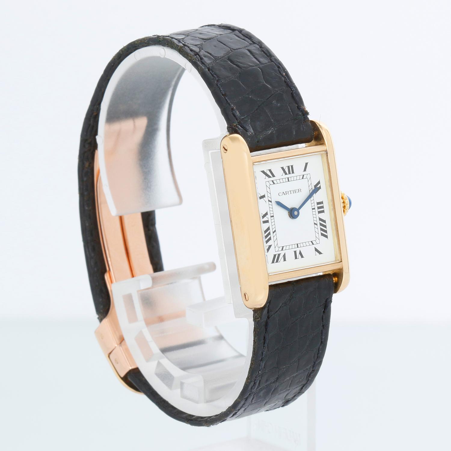 Vintage Cartier Tank 18K Gelbgold Damen  Uhr - Mechanisch. 18K Gelbgold ; blauer Saphir Cabochon in der Krone (24mm Durchmesser). Weißes Zifferblatt mit schwarzen römischen Ziffern. Schwarzes Cartier Armband mit Cartier 18k  Faltschließe. Pre-owned