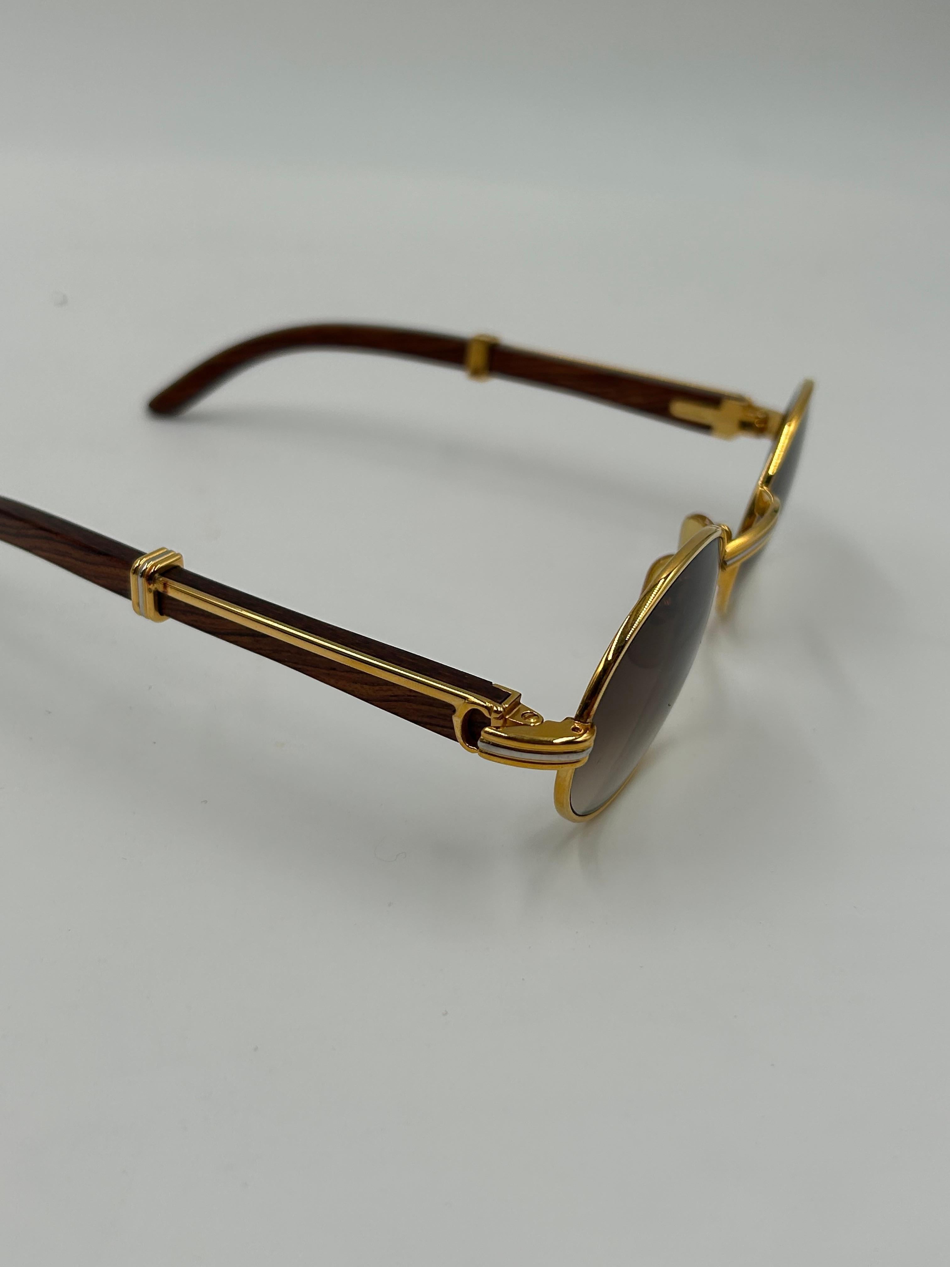 Diese seltene und luxuriöse Vintage-Sonnenbrille von Cartier Auteuil zeichnet sich durch eine einzigartige Kombination aus Edelholzbügeln und goldfarbenen Metalldetails aus, die für die charakteristische Eleganz und Handwerkskunst von Cartier