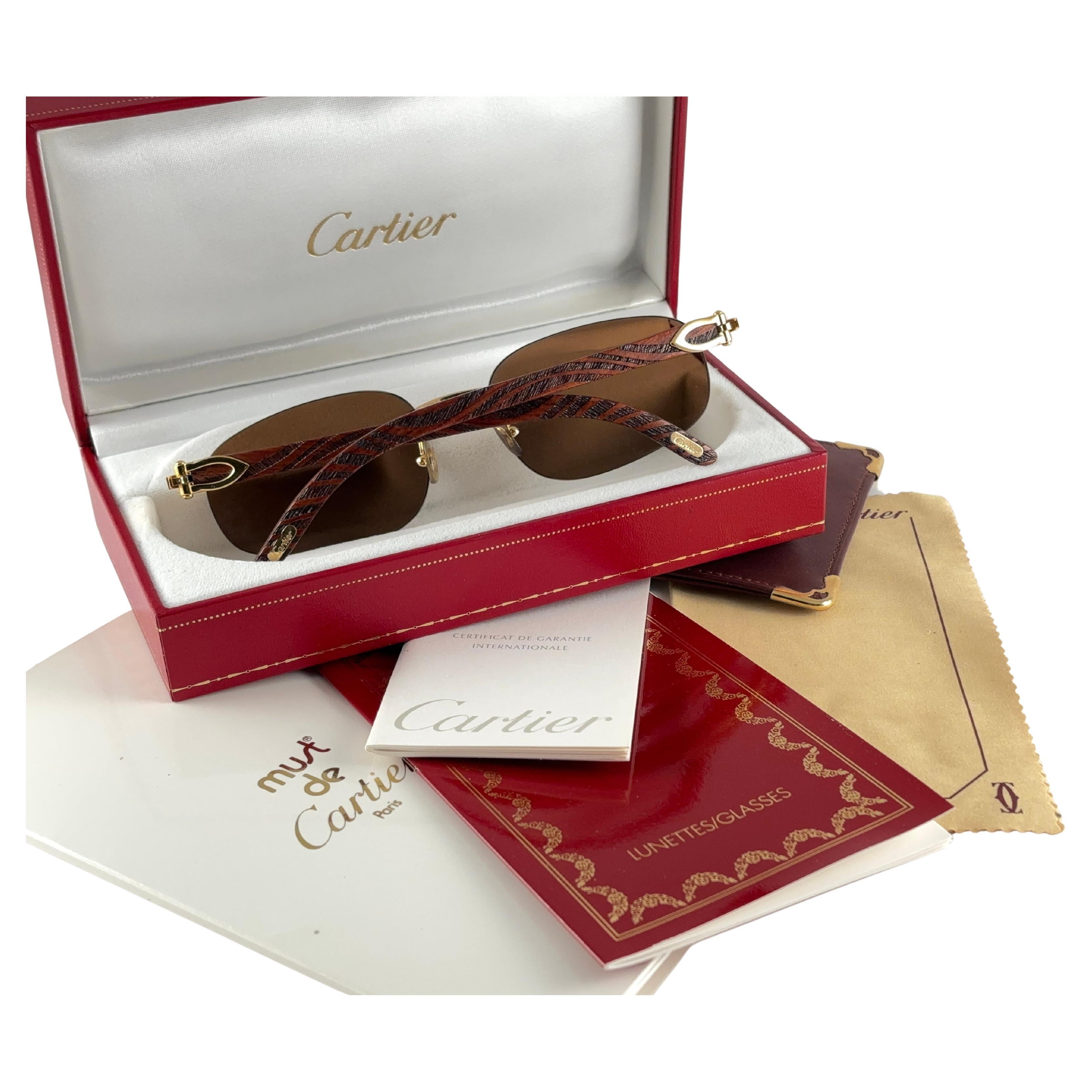 Lunettes de soleil vintage originales de Cartier avec branches en bois sculpté et verres de protection contre les rayons ultraviolets de couleur marron.  
Cadre avec face et côtés en C.C. plaqué or 12 carats.
Tous les poinçons.  Signes Cartier en or