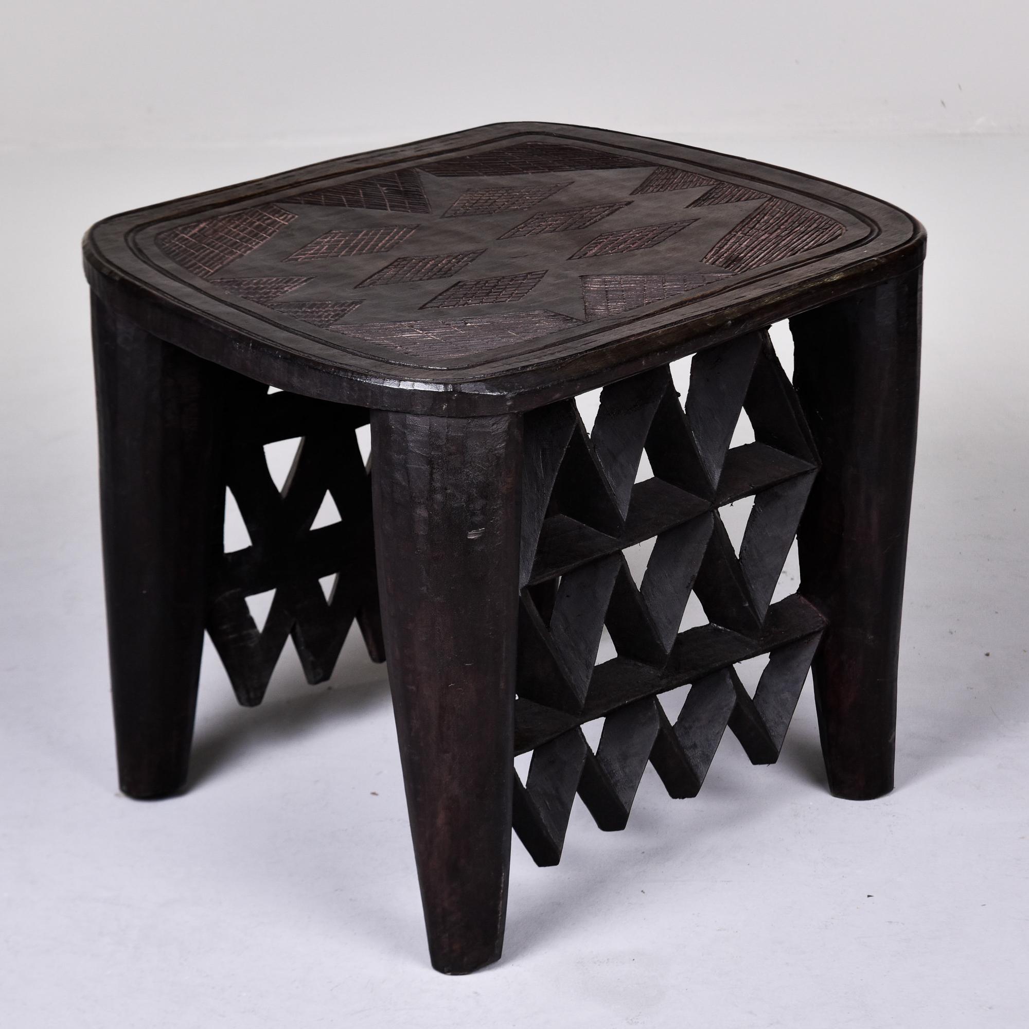Circa 1960s hand carved side table by the Nupe people of Nigeria. Dark, dense wood has been hand carved from one solid piece. Four thick rounded and tapered legs with open lattice work sides. Carved designs on table top. Overall very good vintage