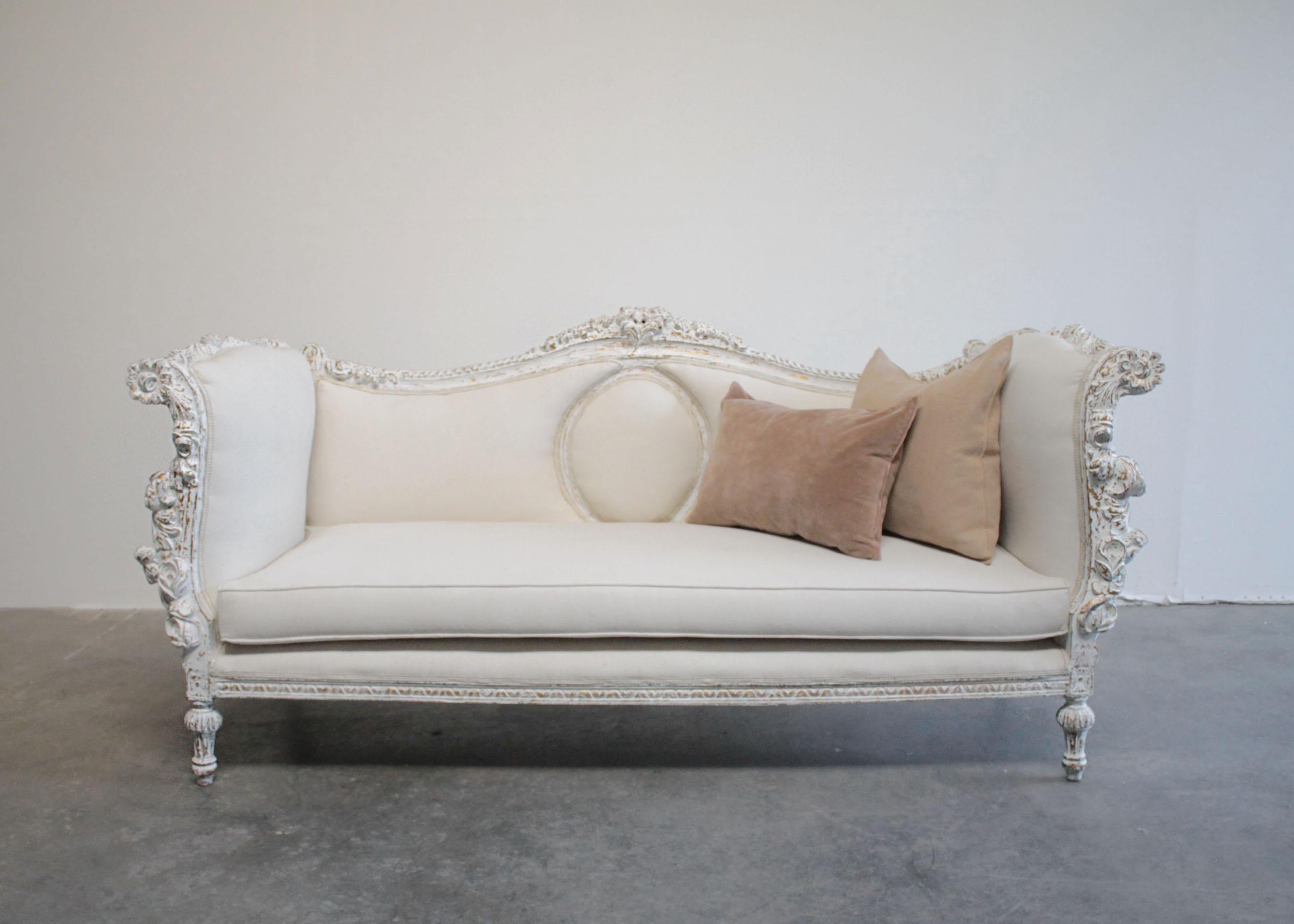 Vintage carved and painted French style sofa 
Large floral carved sofa, painted in a French antique white with distressed edges, where gilt and wood are showing through the paint.
Trailing garlands of flowers and scrolls across the back. Fluted