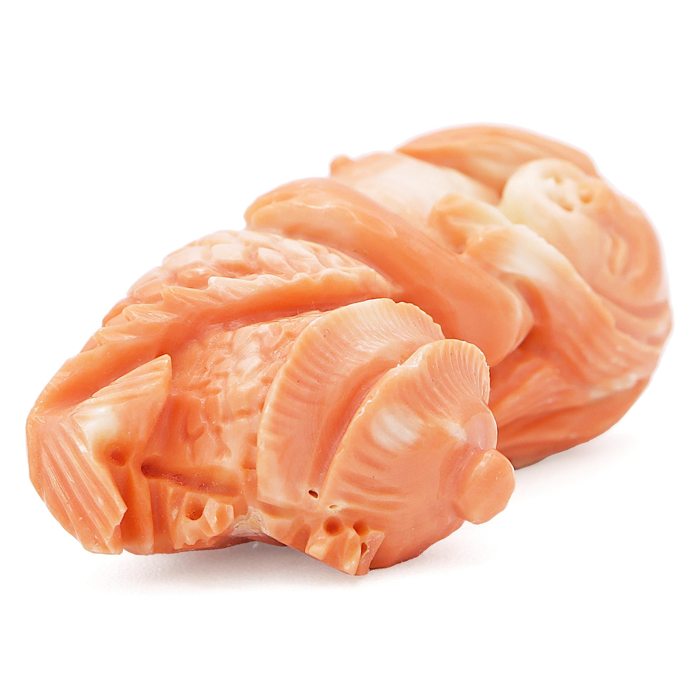 A charming coral sculpture. Crafted from coral, this piece depicts a serene mermaid with flowing hair and a gentle smile. The mermaid's tail is intricately detailed with scales, leading to a textured shell-like structure at the end. A captivating