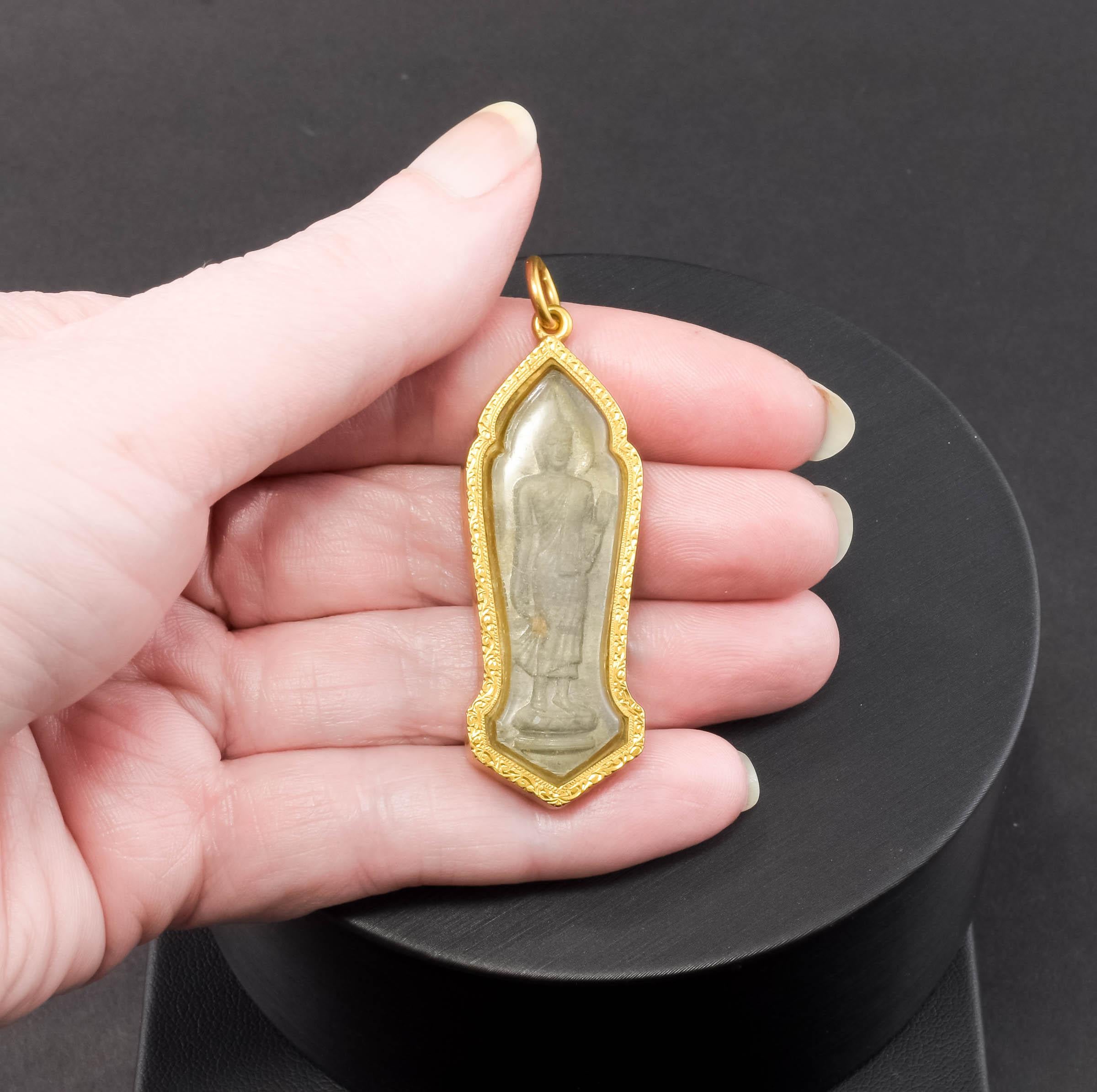 Offered is a particularly beautiful pendant featuring a carved stone Buddha under glass, within a decorative high karat gold frame. The research I have done tells me that this amulet or reliquary is based on a Sukhothai period Buddha. (please note