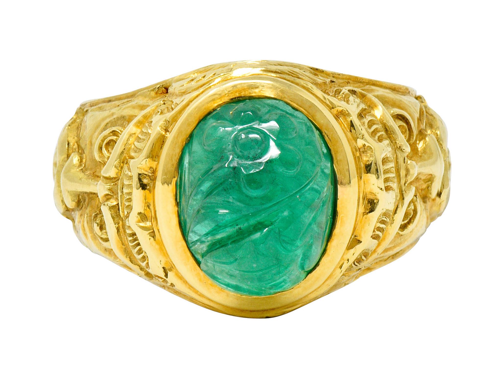 Statement ring centers an oval cut emerald cabochon measuring approximately 11.5 x 9.1 mm

Semi-transparent with bright green color and deeply carved to depict flourishing florals

Bezel set with highly rendered shoulders depicting stylized Green