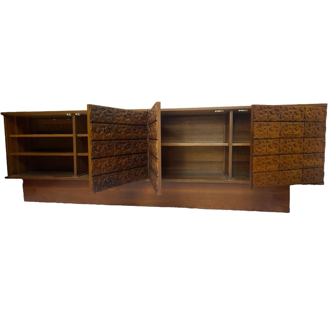 A custom two-part walnut cabinet set on a plinth base, featuring intricately carved doors resembling tooled leather and a beautifully grained smooth walnut top, sides and interior finish. Designed for both style and utility, the top back edge is