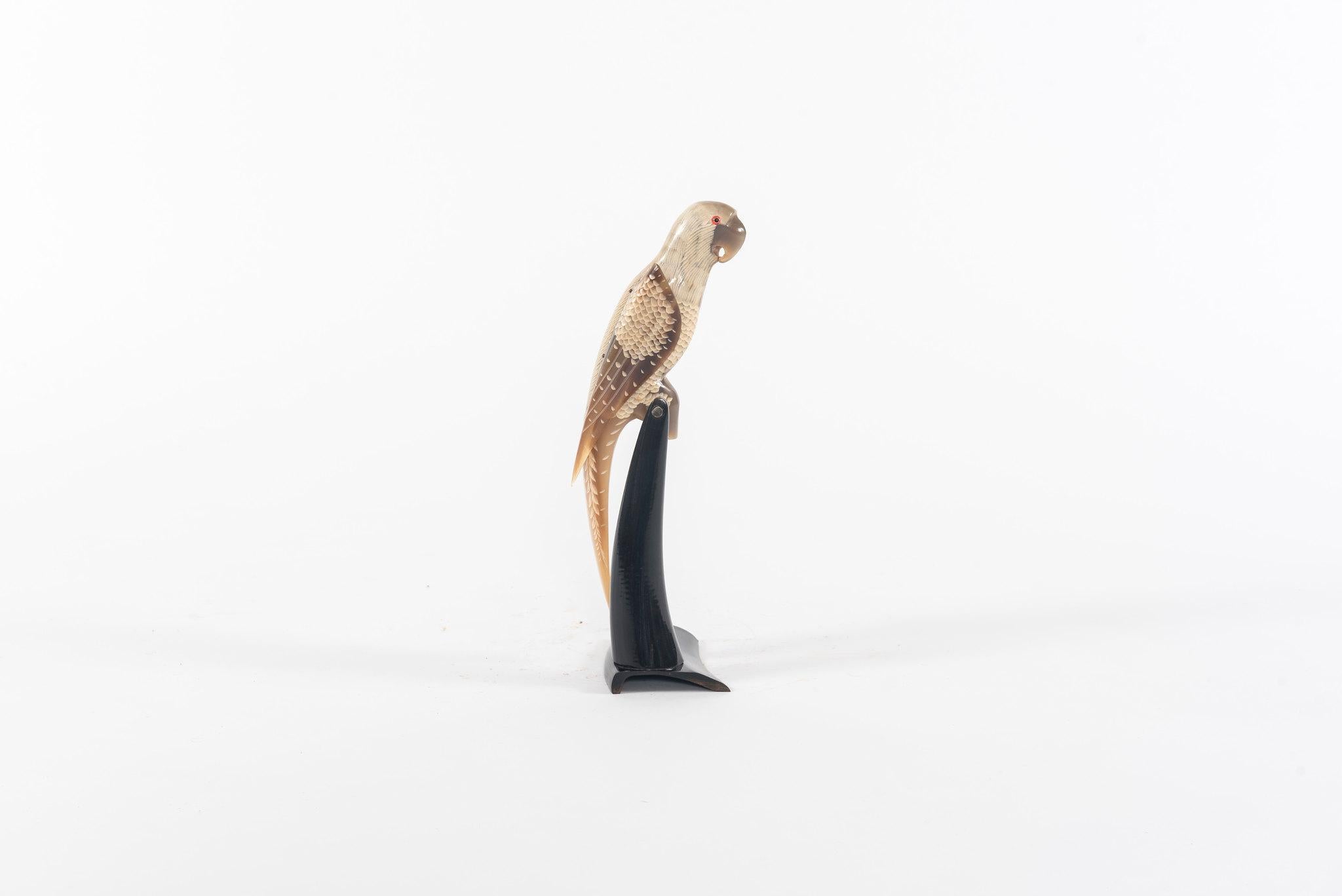 A beautifully hand carved water buffalo horn parrot. This parrot is caramel and creamy in color and is perched on a black horn stand.