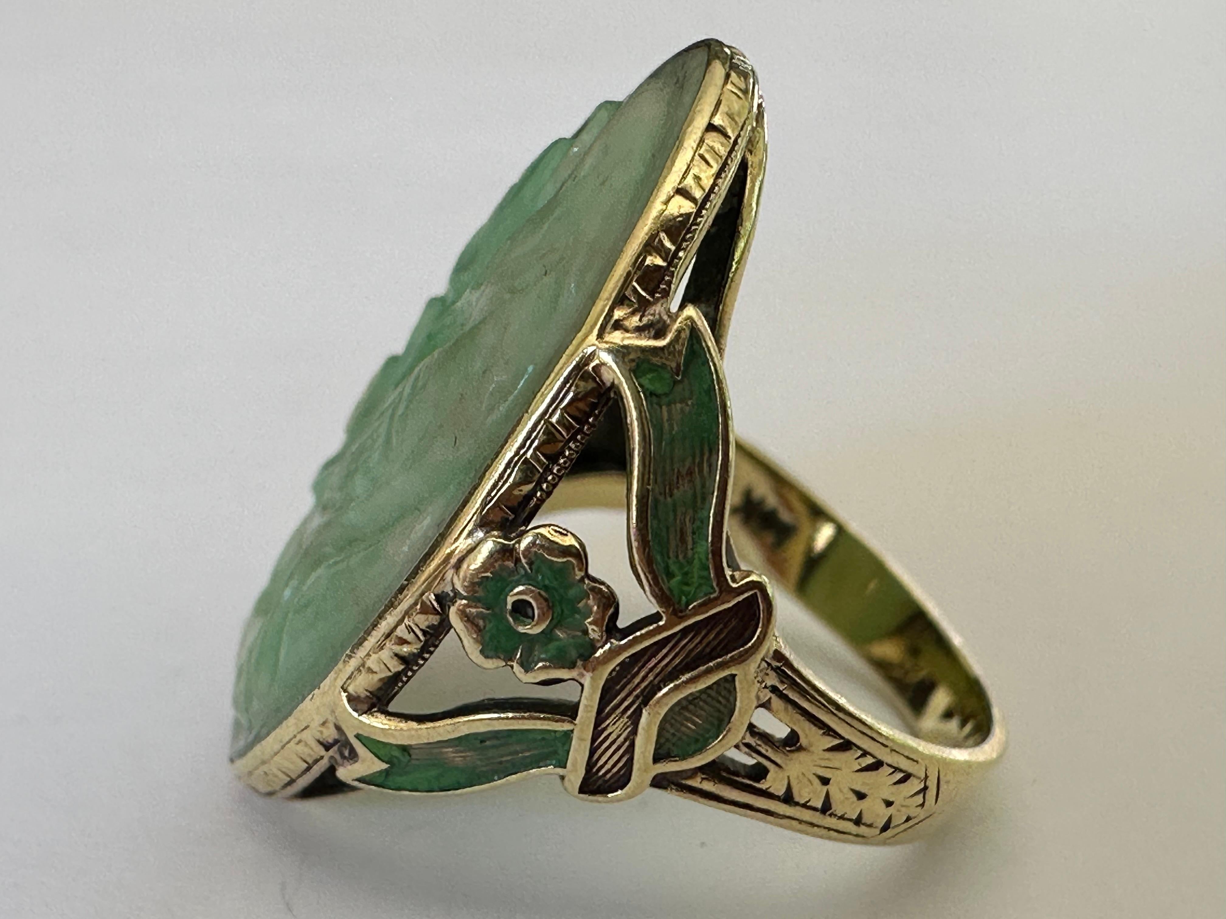 Questo anello vintage di metà secolo è disegnato attorno a una placca di giadeite intagliata di forma ovale, impreziosita su ogni lato da accenti di smalto verde a motivo floreale. Incastonato in oro giallo 14 carati. 
