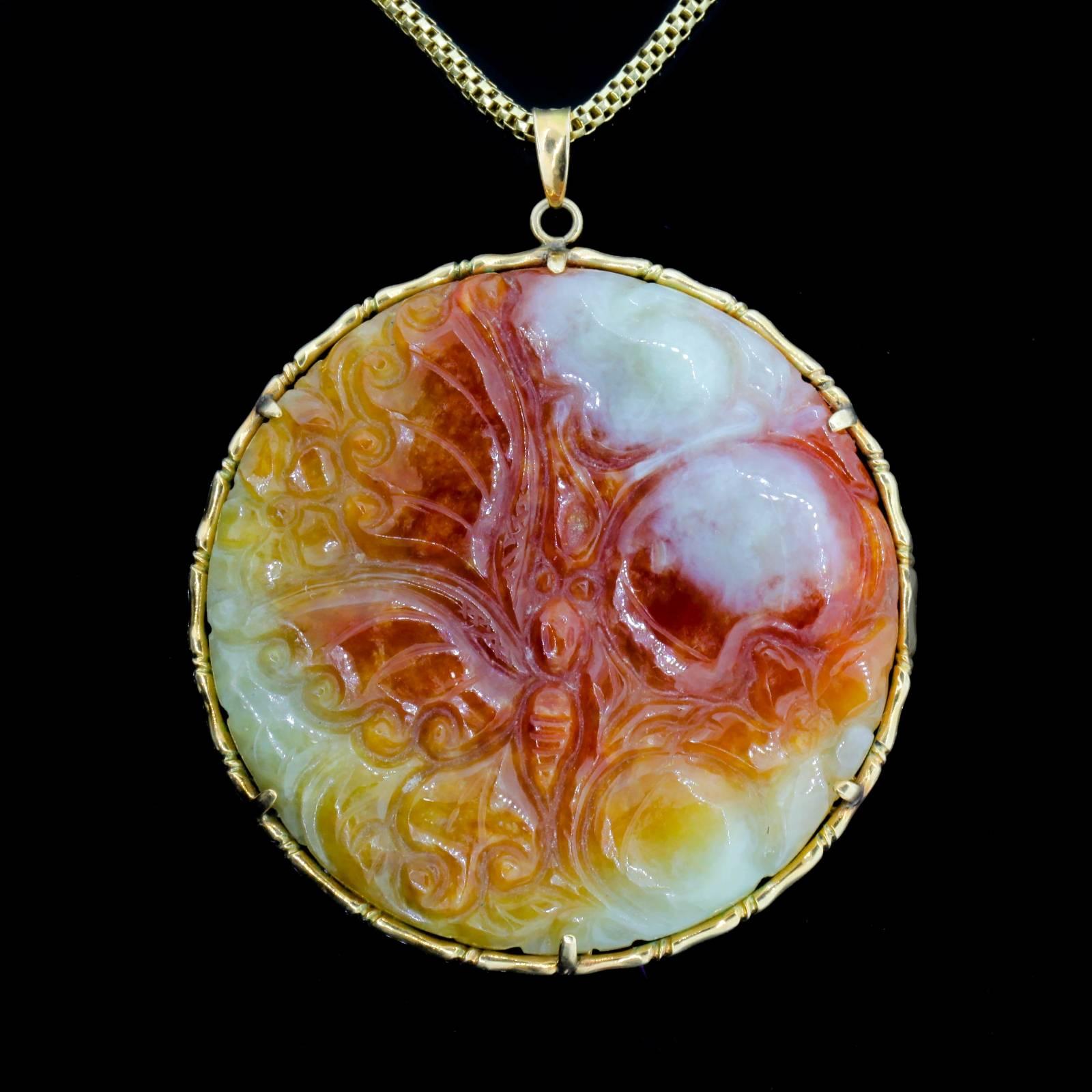 A 1960s carved Jadeite circular plaque with a butterfly and floral motif in mottled colors of brownish-red, gold, yellow and white.  The pendant is set in a bamboo design 14KT yellow gold frame, and measures 2 1/4 inches in diameter, suspended from