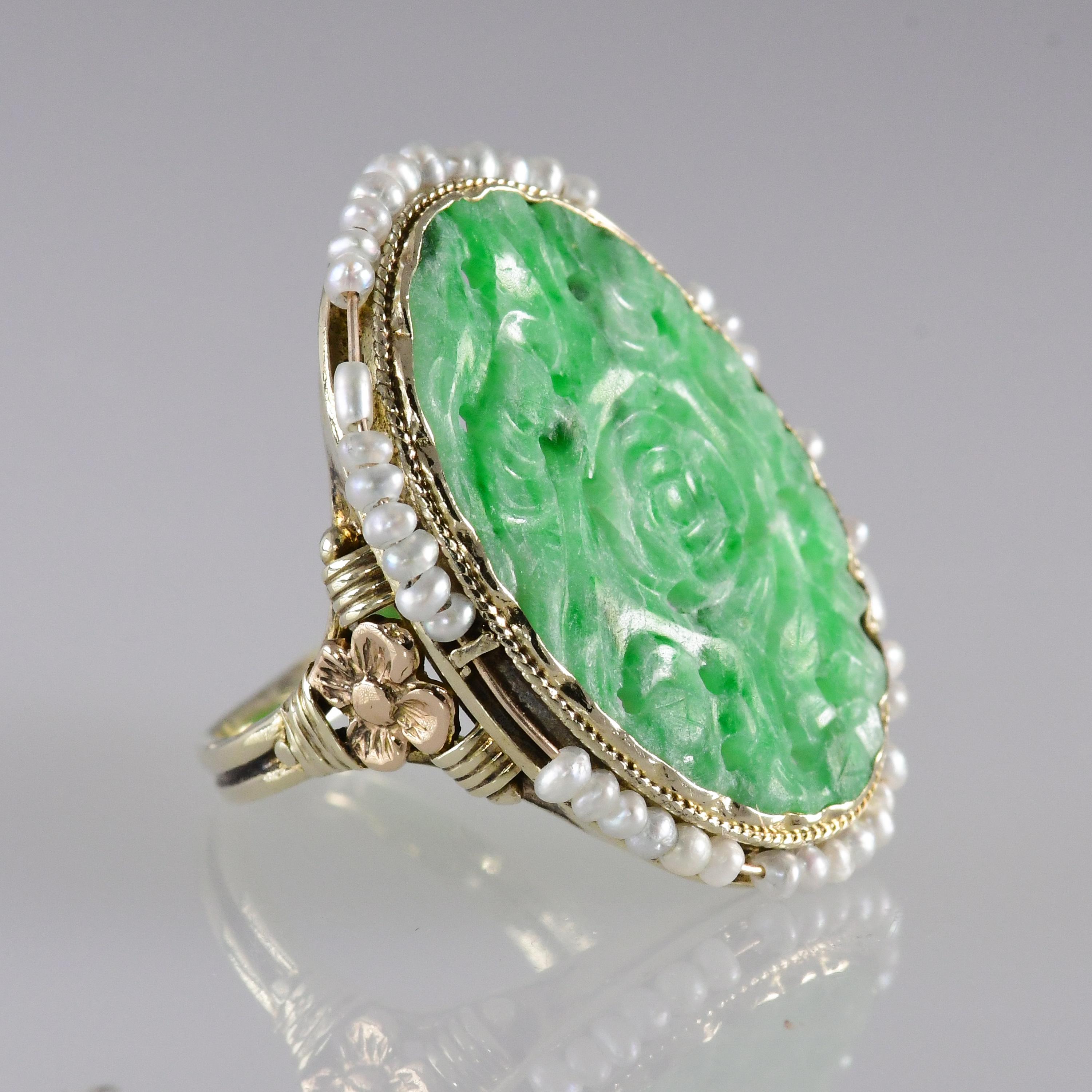 1920's carved jadeite ring encircled with seed pearls. The 14 karat yellow gold ring is enhanced with a rose gold floral design on the ring shank. 
The jade measures approximately 23 millimeters long (.90 inch) and 15.5 millimeters (.61 inch) . The