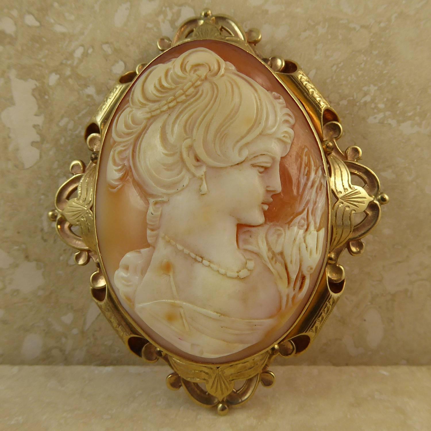 A vintage cameo brooch from 1965 in an imposing size and with an impressive sculptural gold frame.  The cameo depicts an attractive woman in profile against the amber background of the conch shell.  She appears to be in a contemplative mood and has
