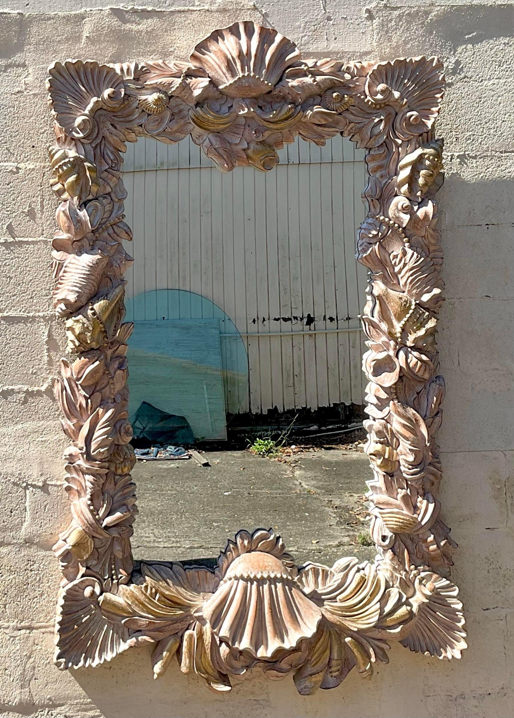 Dieser Spiegel mit geschnitzten Muscheln und Perlen im Vintage-Stil fängt das Wesen der Schönheit der Küste ein. Das filigrane, in amerikanischer Handarbeit gefertigte Design versprüht maritimen Charme und verleiht jedem Raum einen Hauch von
