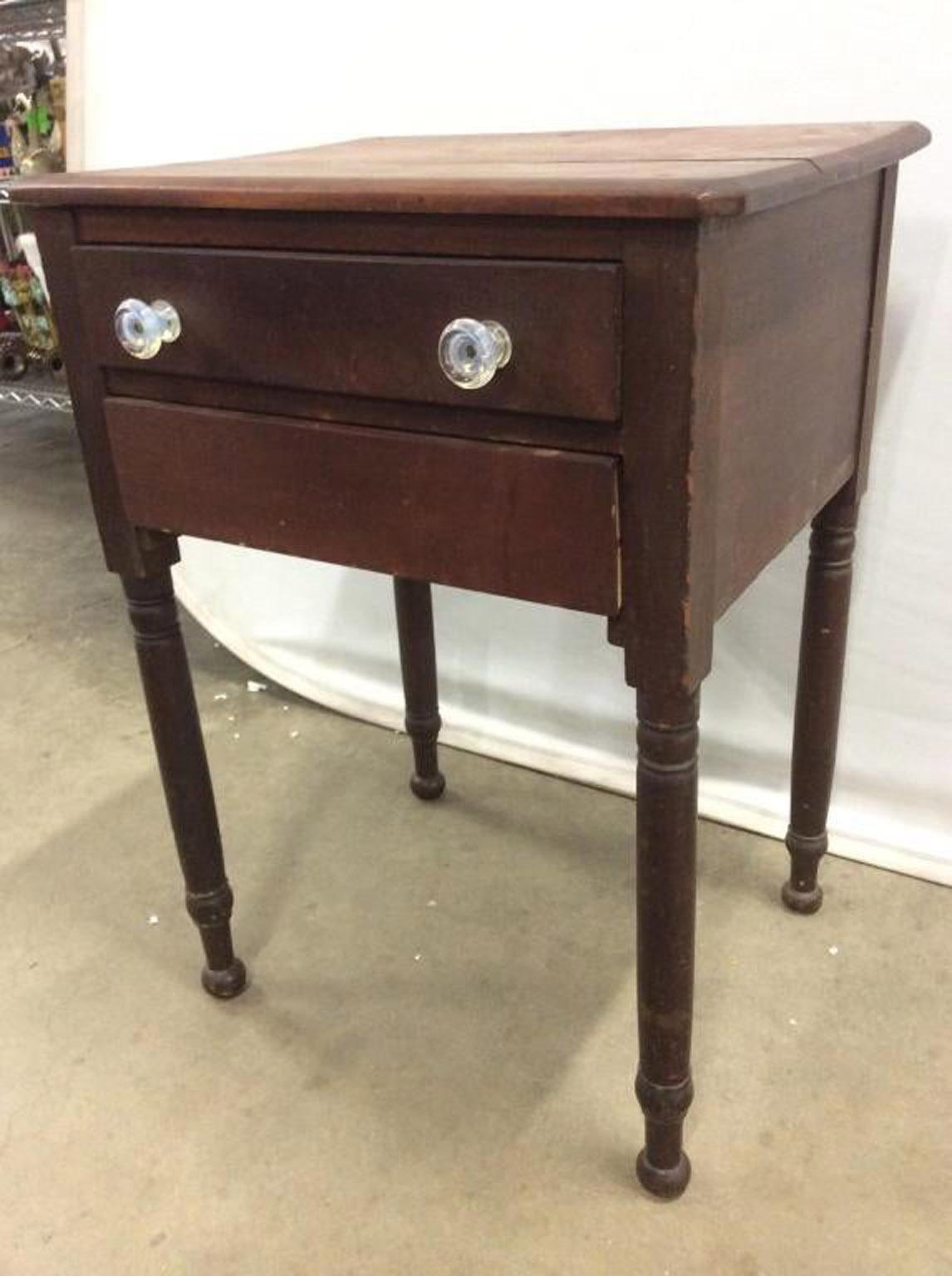 A rustic Sheraton style end table or stand with 2 drawers, and turn legs. Top drawer has 2 handles. Piece contains wear and separation on tabletop. Suitable to use as end table, side table, bedside lamp table.
  