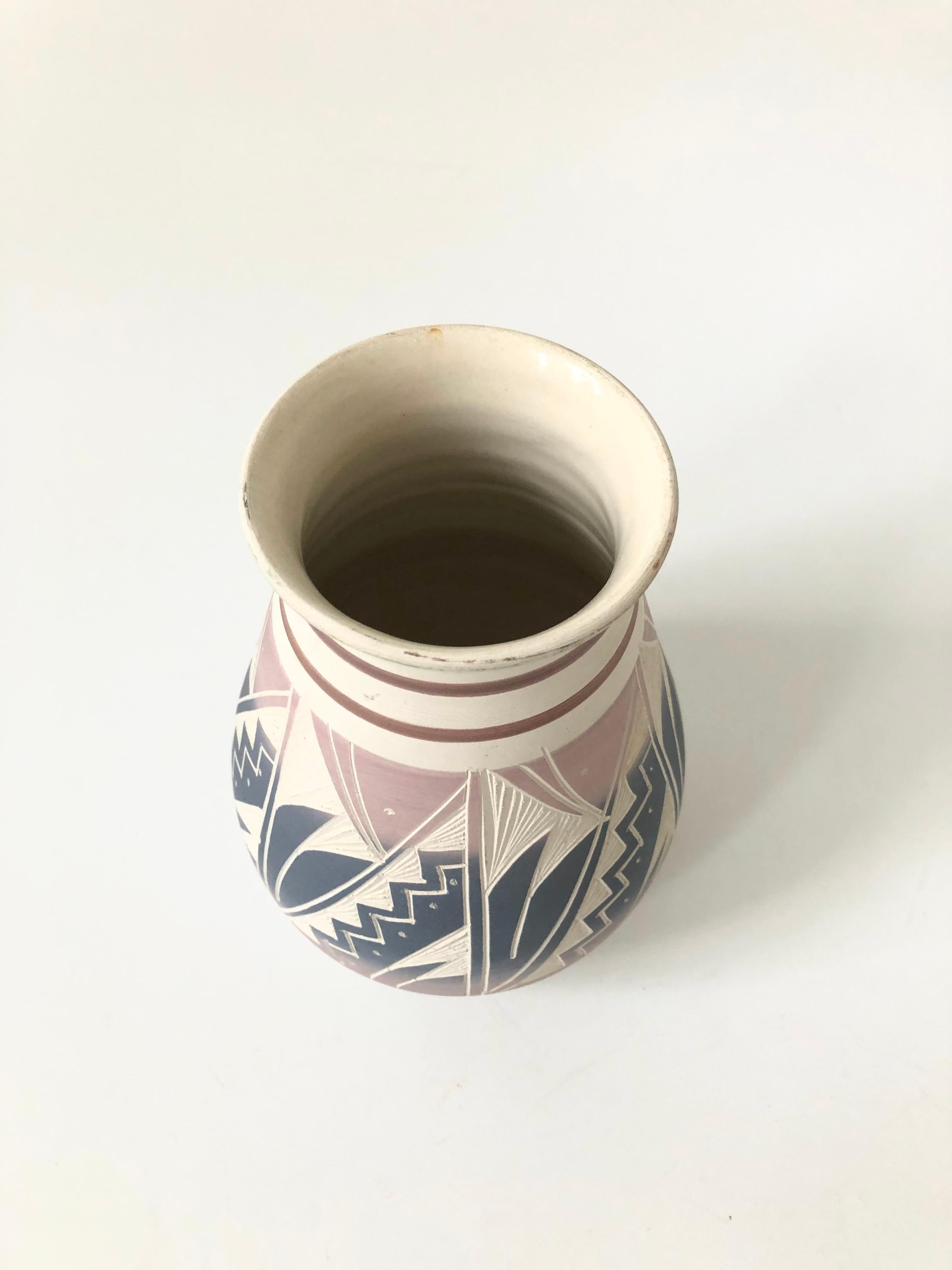 A beautiful vintage hand carved Southwestern pottery vase. Lovely pink and purple glazes over a white base color and a highly detailed geometric pattern that has been hand carved into the sides of the vase. Signed on the base by the maker.
  