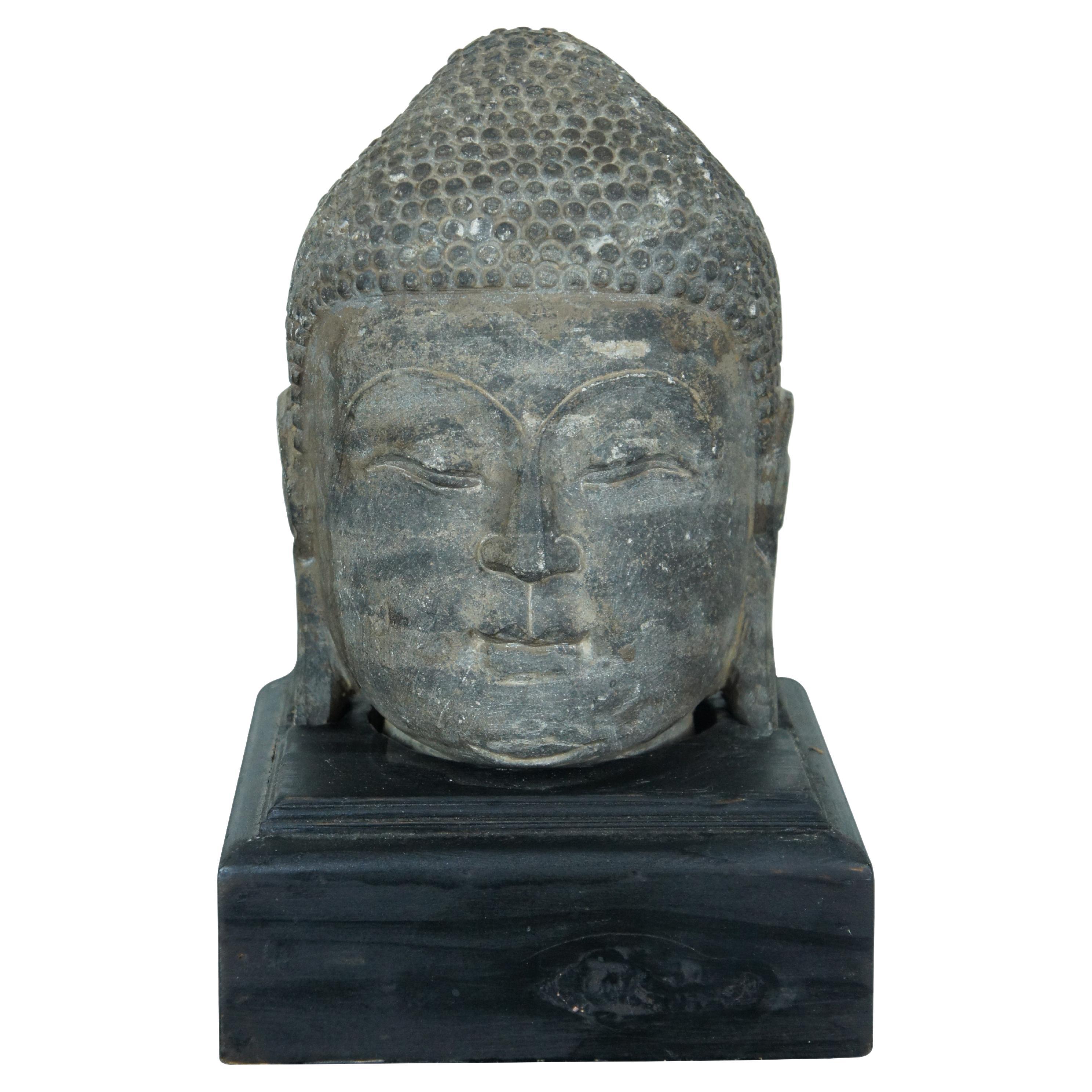 Pesante  scultura / statua in pietra scolpita con testa di Buddha, capelli arricciati, orecchie allungate, occhi chiusi ed espressione leggermente sorridente. Incastonato in un piedistallo di legno dipinto di nero.

Dimensioni:

7