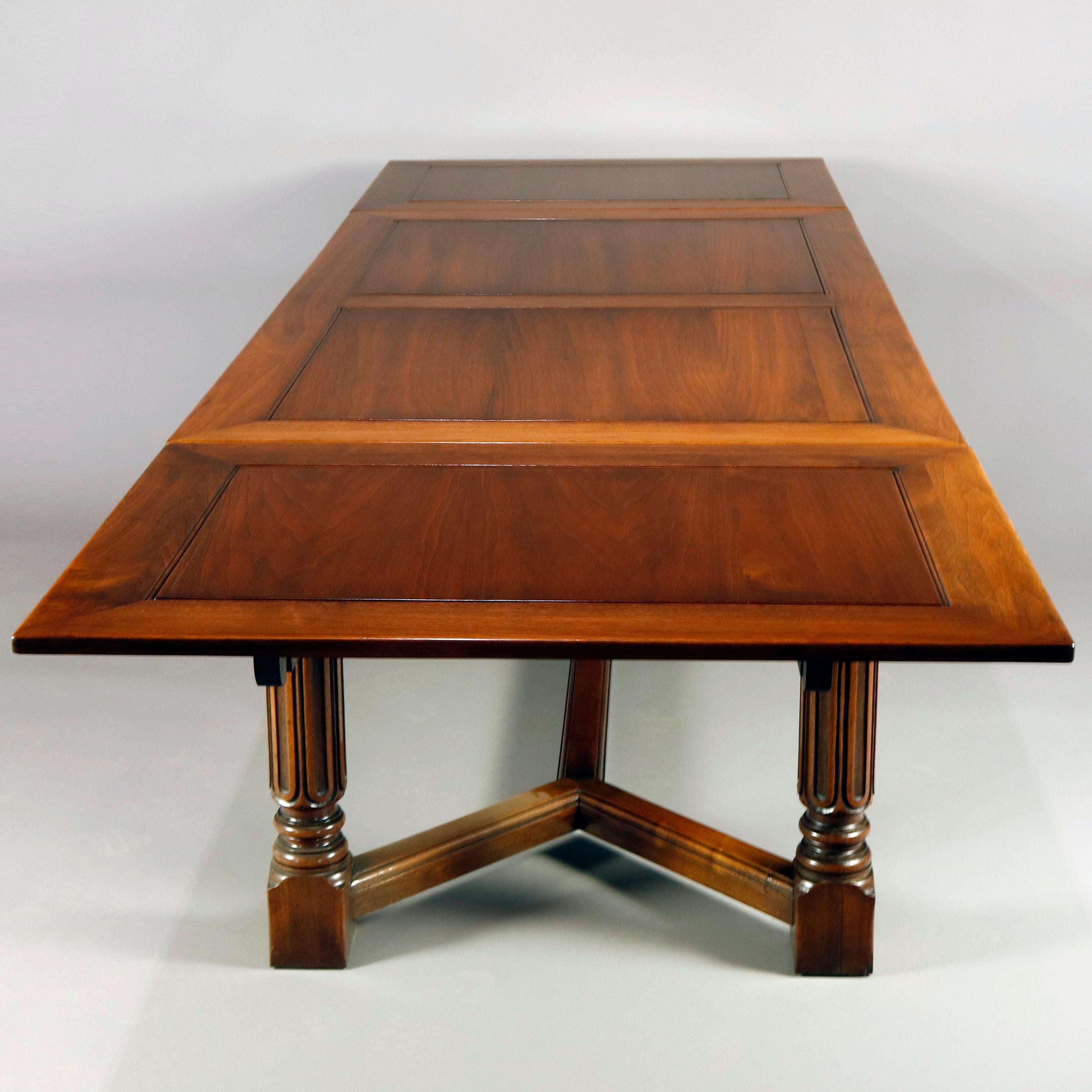 A vintage Gothic style Kittinger draw top dining table features heavily carved walnut construction with cross banded top surmounting apron with carved foliate and geometric decoration and raised on turned and reeded legs with trestle style
