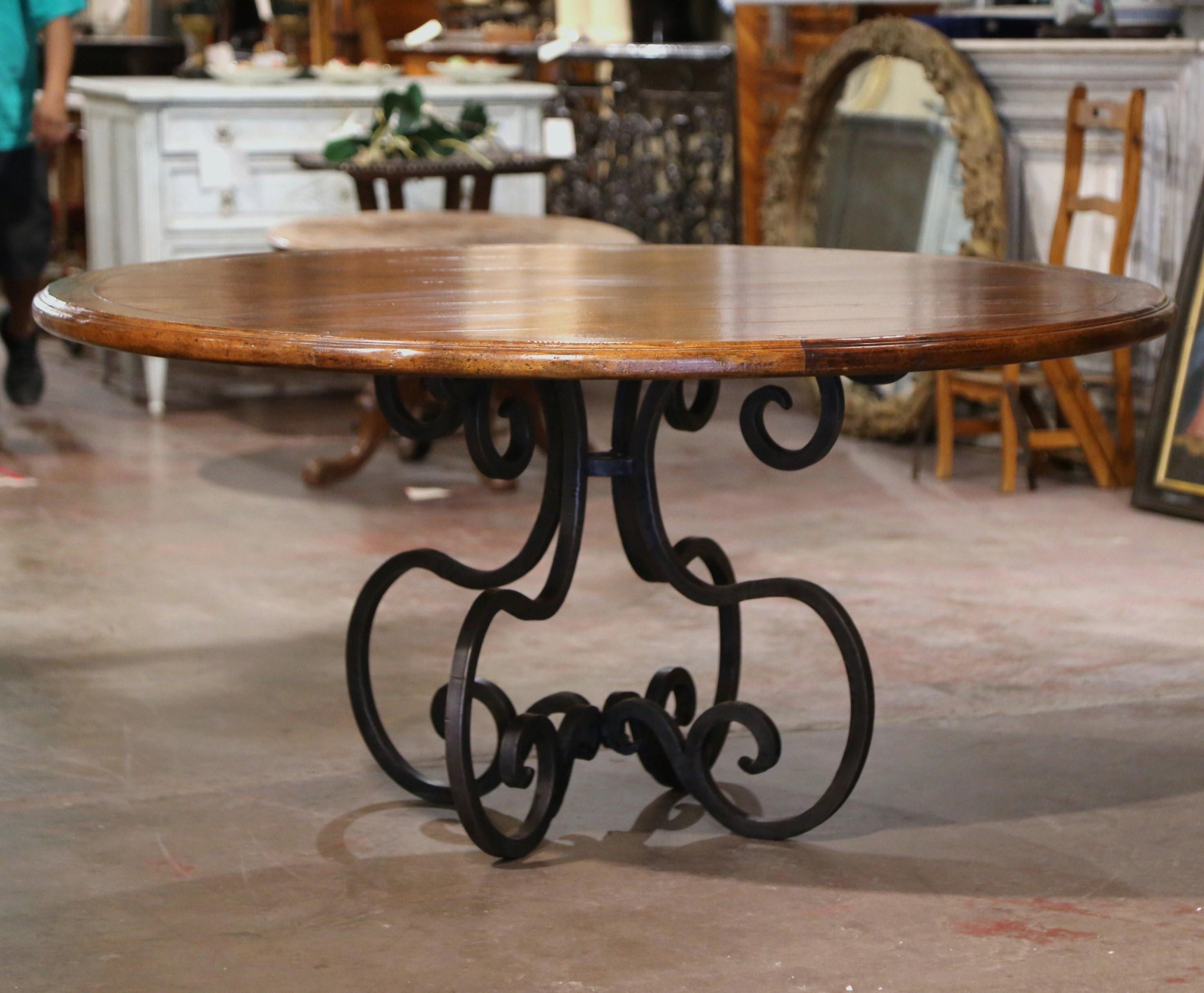 Crafted in the USA circa 1980, the elegant table stands on forged wrought iron base with scrolled legs. Almost 5 feet in diameter, the circular wooden top features old walnut planks set inside a round frame. The large round table is in excellent